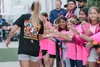 A group of young girls in pink shirts giving a high five to a woman with long blonde hair wearing a black T-shirt, at an outdoor event.