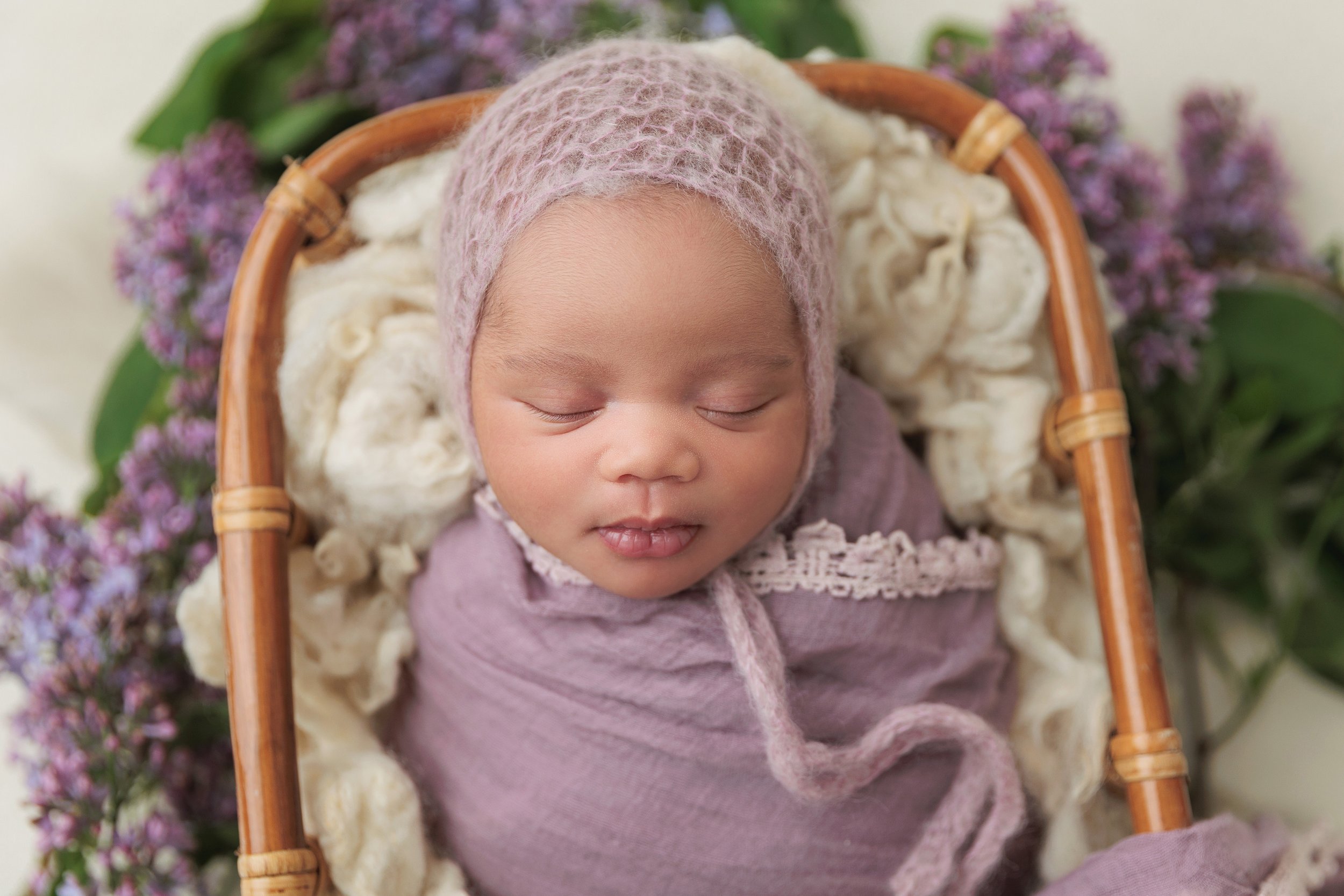 newborn baby girl in purple set up with fresh lilacs