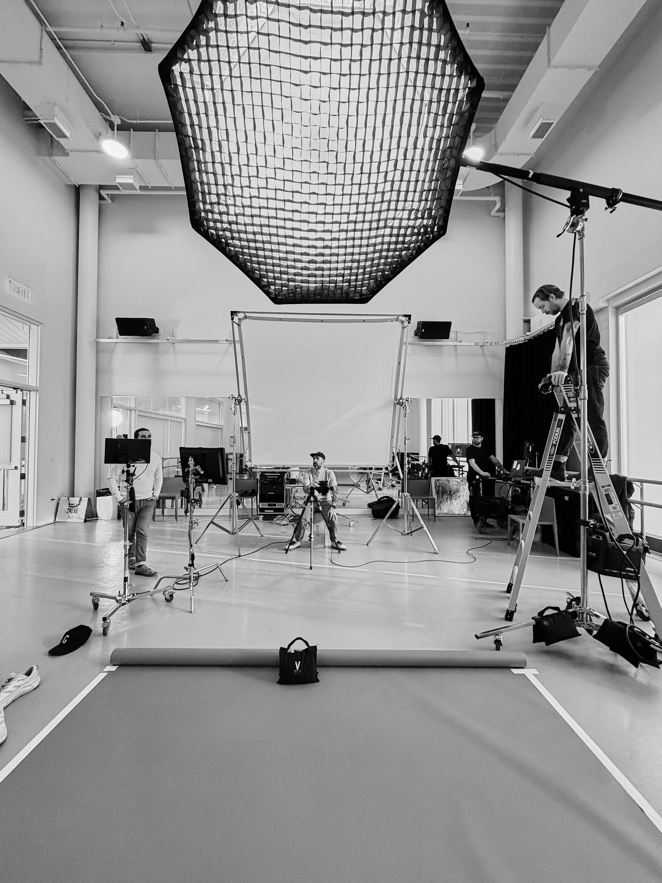 Behind-the-scenes view of a photography or video set with lighting, camera equipment, and crew members preparing in a studio.