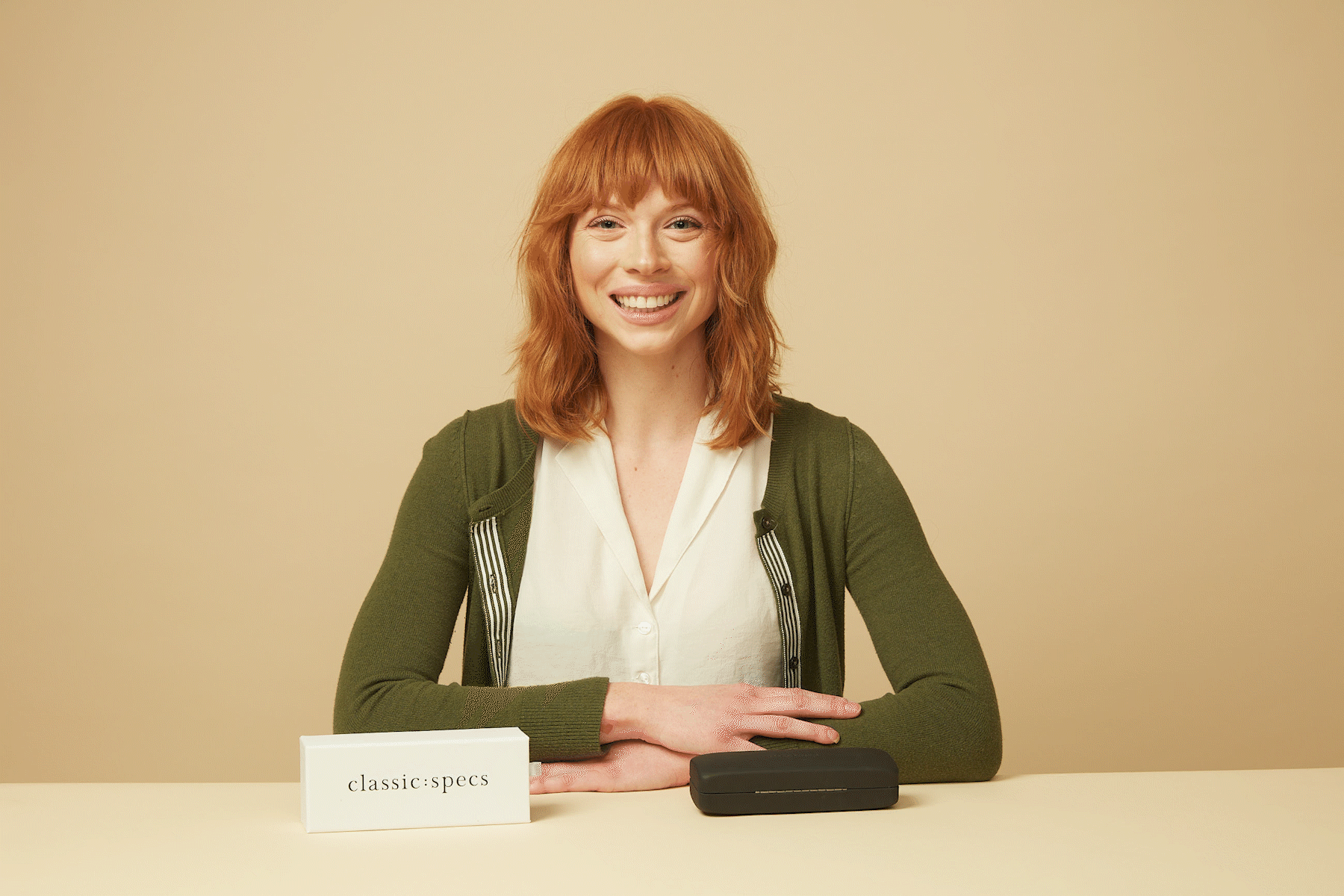 Woman with red hair smiling at a table with a black case and a sign that says "classic:specs"