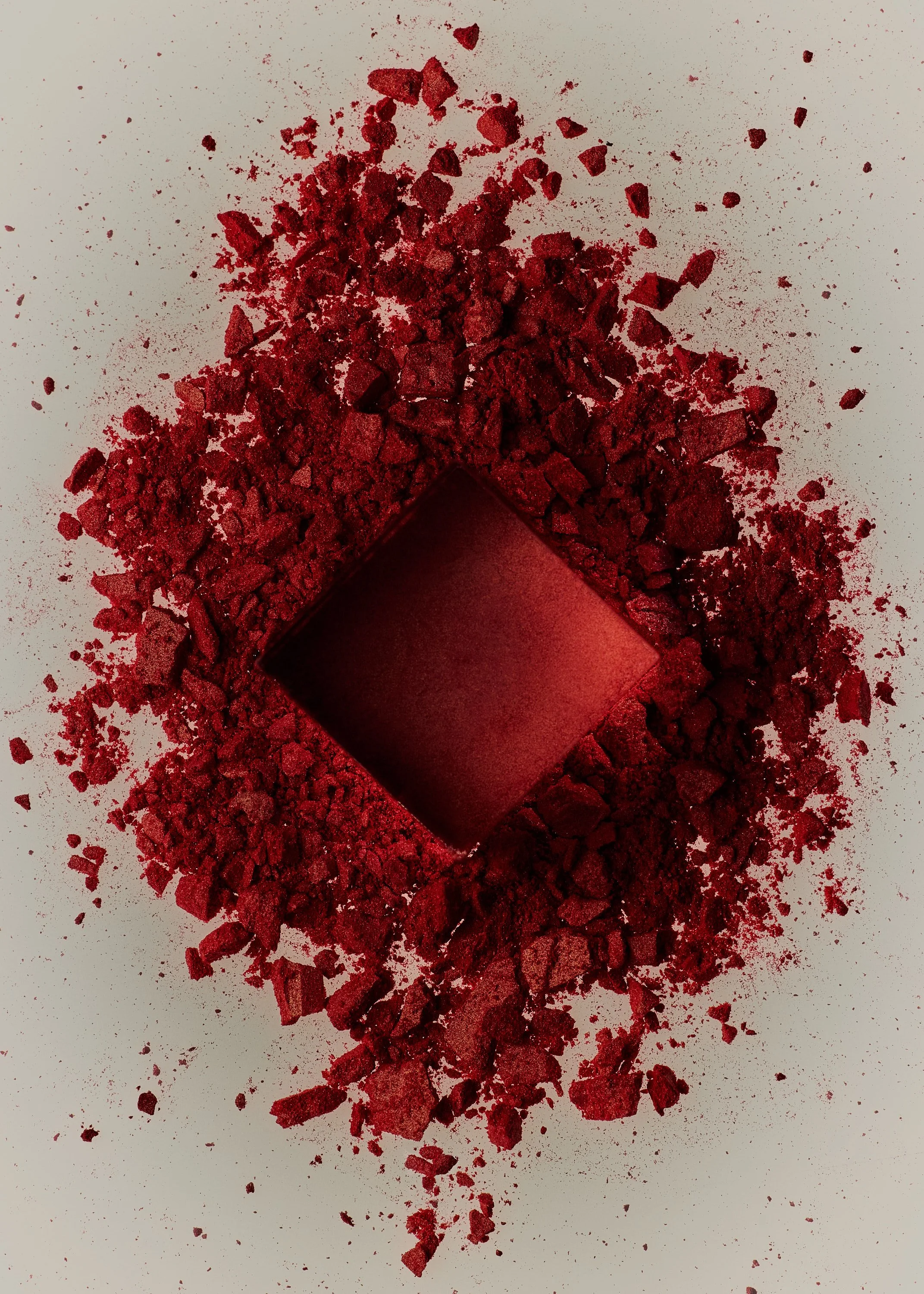 Red eyeshadow pigment powder with a square-shaped compact in the center on a light surface.
