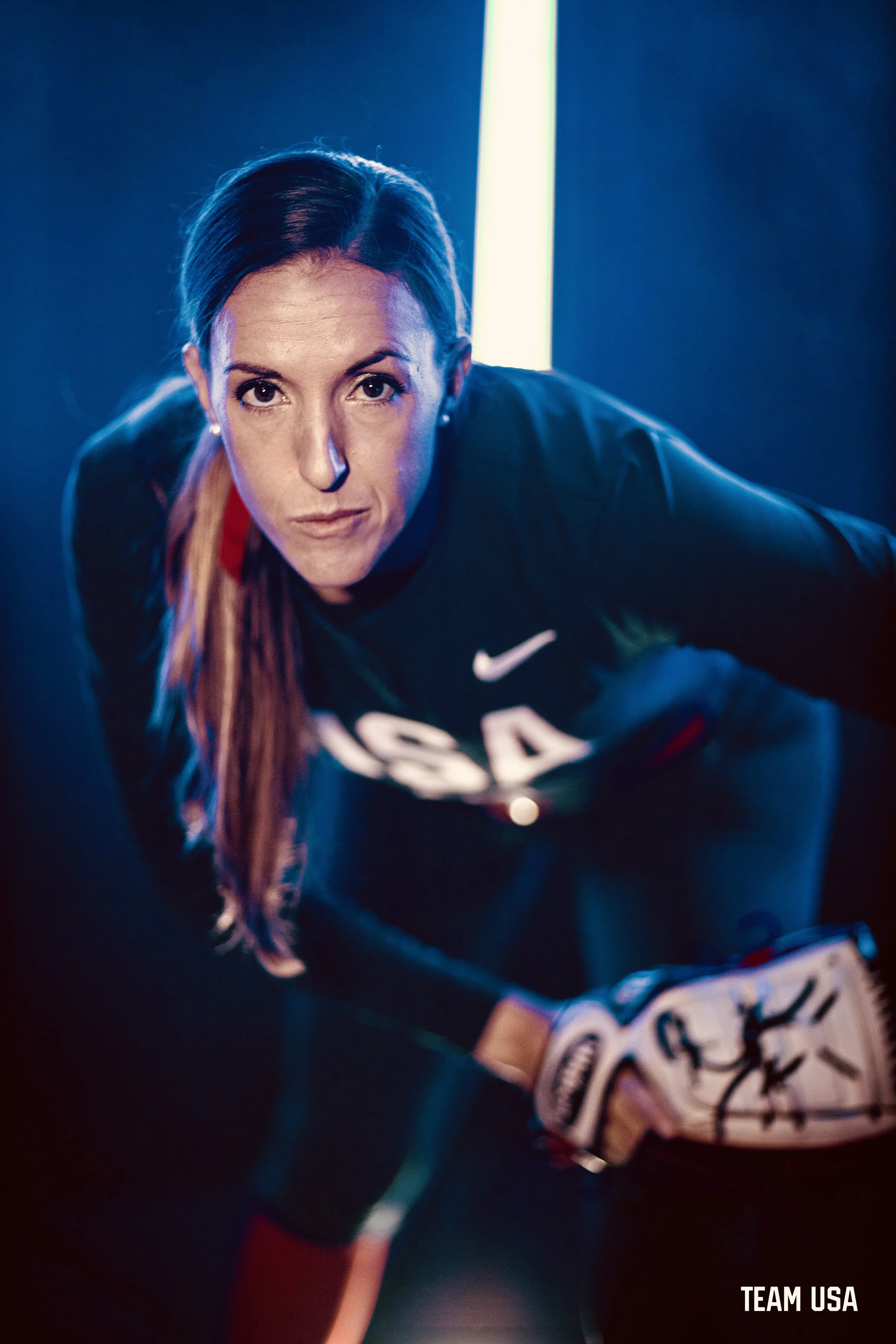 Female athlete from team USA, in an athletic position with her game face on  in a dimly lit environment. "Team USA" text is visible in the corner.