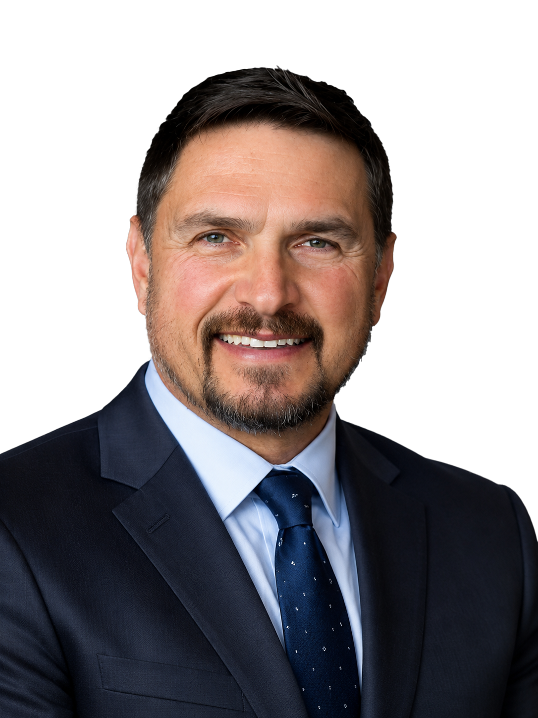 Headshot of a middle-aged man with dark hair, light beard, wearing a navy suit, white shirt, and dark tie, smiling against a white background.