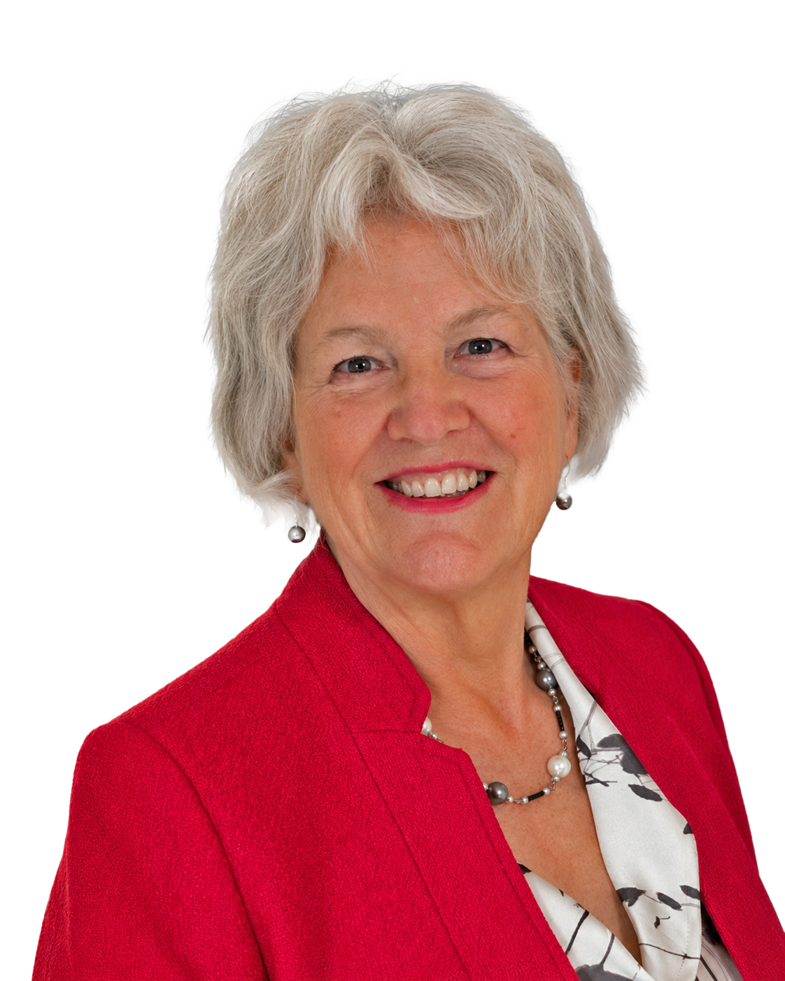 A woman with gray hair wearing a red blazer, patterned blouse, and pearl jewelry, smiling at the camera.