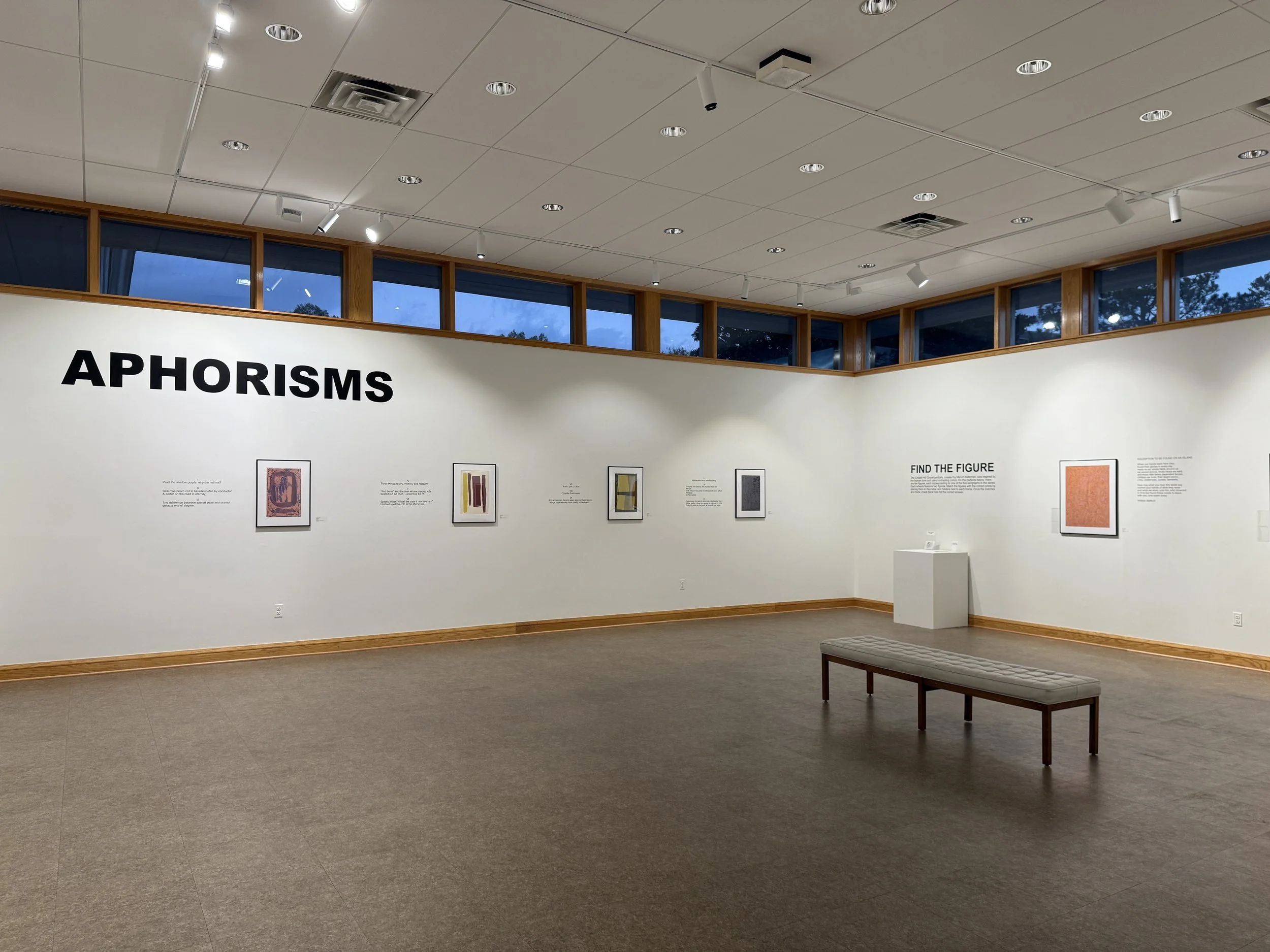 Commons Gallery view of serigraphs by Marvin Saltzman and "Aphorisms" in large text on the wall