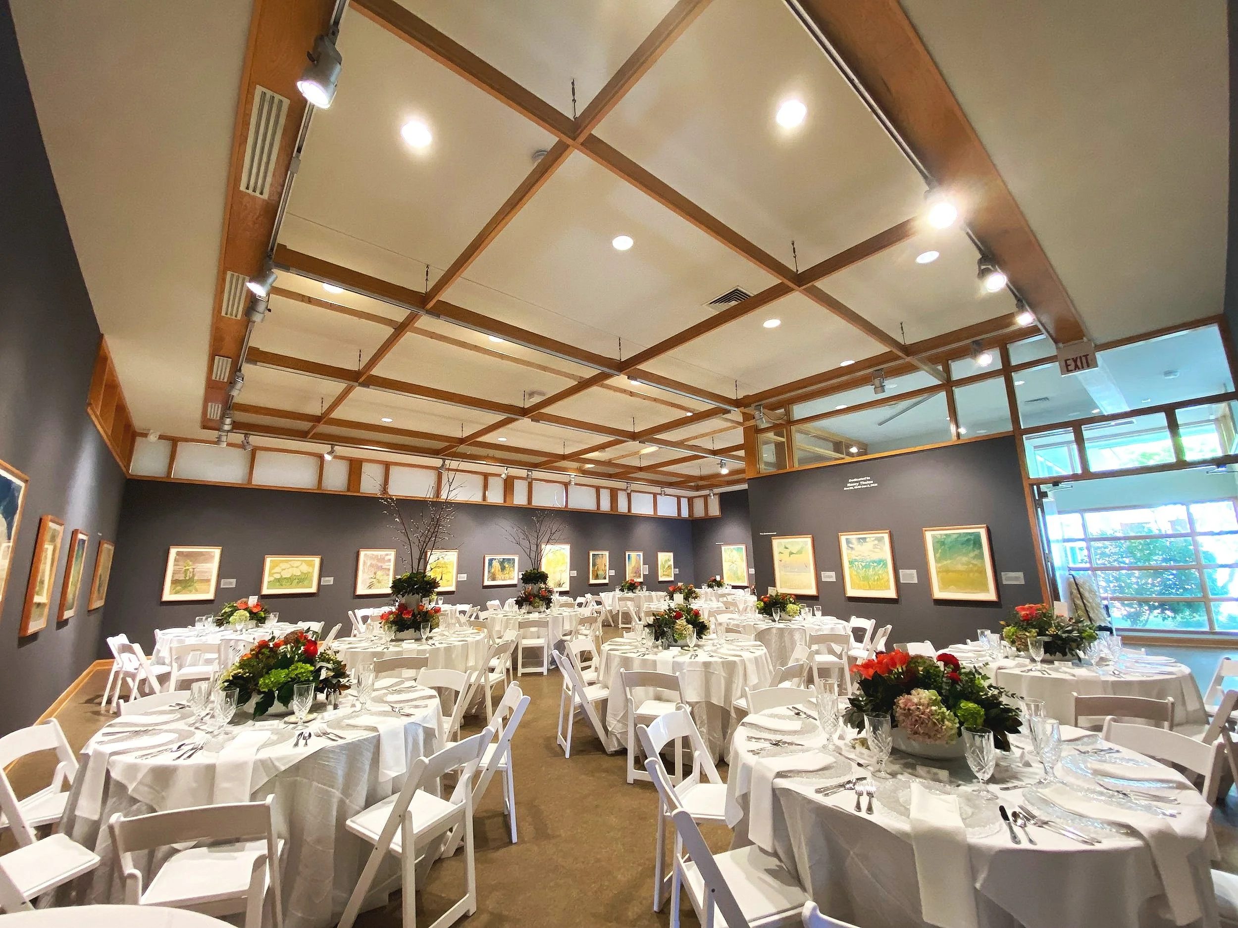 gallery setup with white round tables, chairs, floral arrangements, and dinnerware