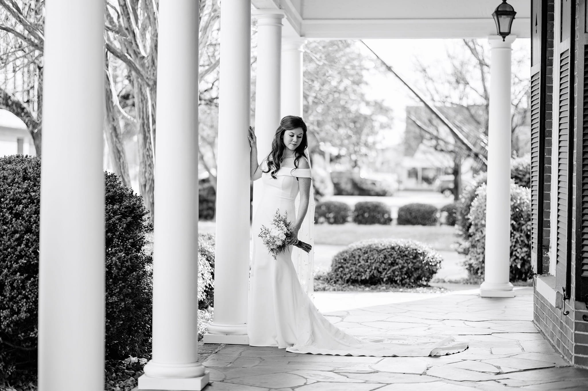 black and white photo of bride in dress on historic front porch of the museum
