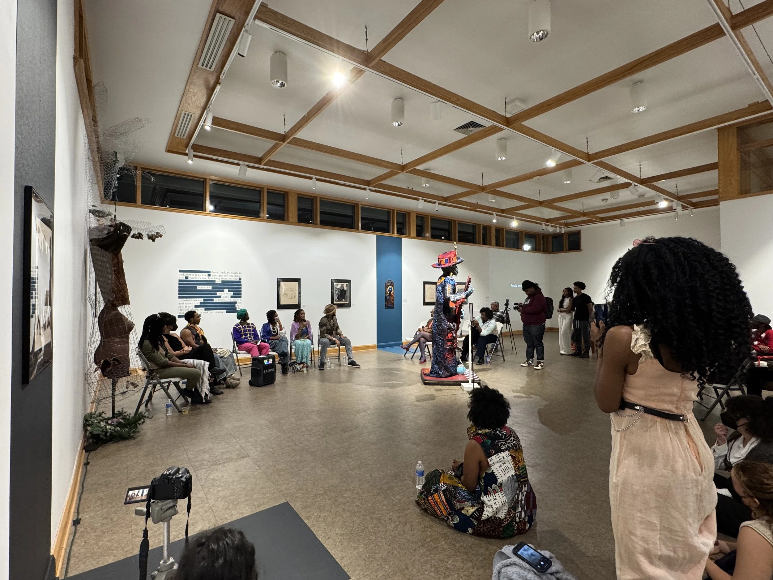 crowd of people standing in gallery with artists seated in a semi circle