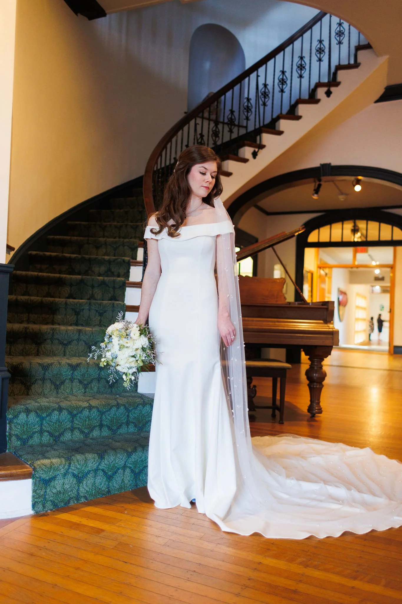bride in white holding flowers and standing in front of historic spiral staircase in museum