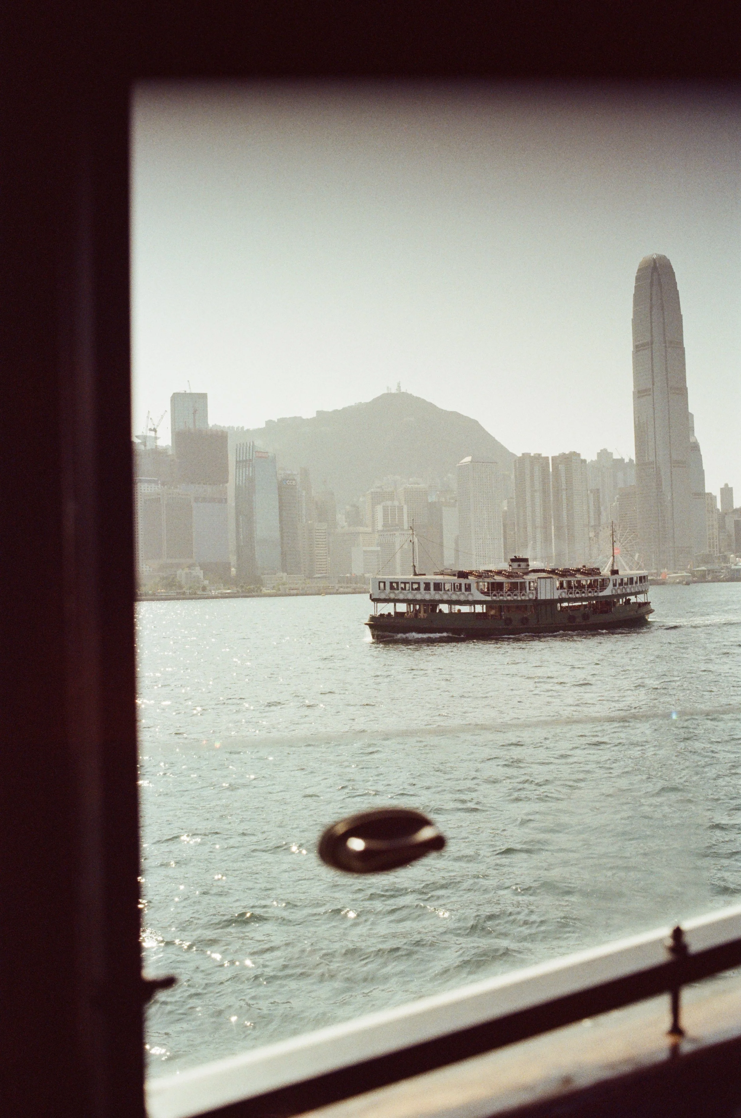 A boat on the water with a city skyline, including tall buildings and mountains, in the background.