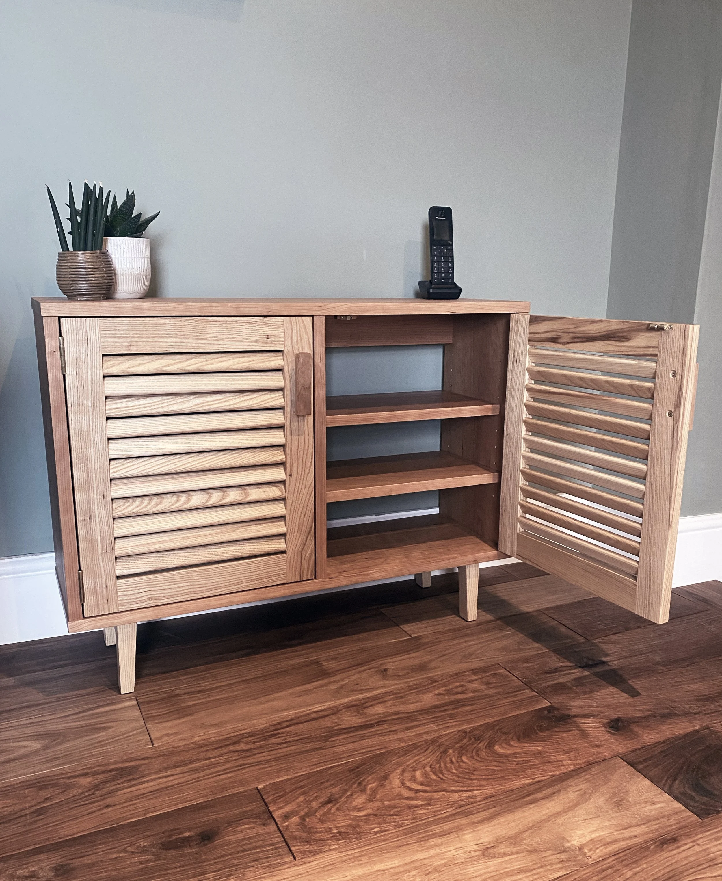 A contemporary oak and cherry cabinet with louvred doors, featuring clean lines and an elegant, understated design.