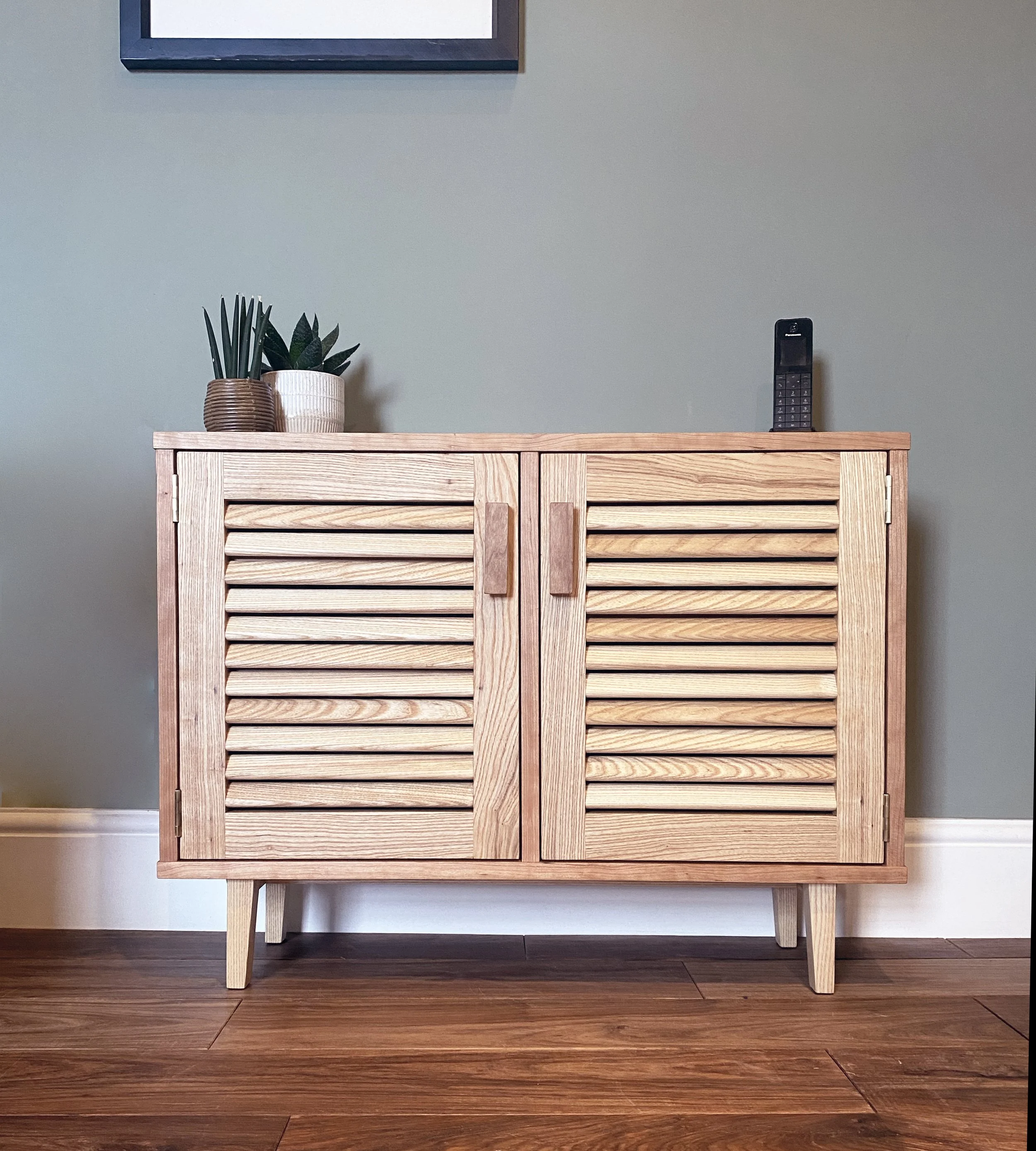 A contemporary oak and cherry cabinet with louvred doors, featuring clean lines and an elegant, understated design.