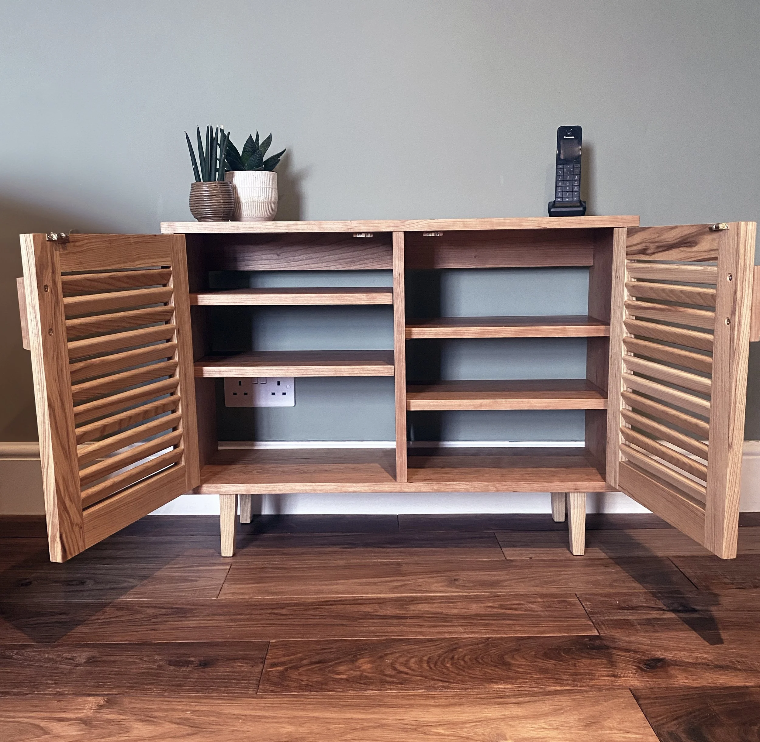 A contemporary oak and cherry cabinet with louvred doors, featuring clean lines and an elegant, understated design.