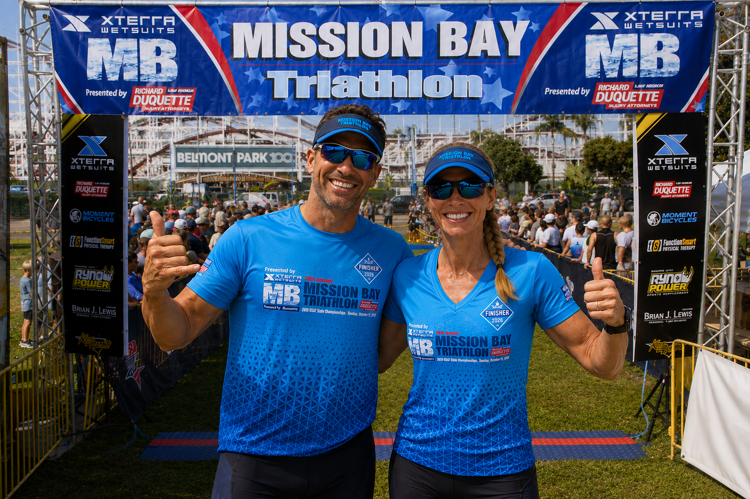 Two athletes wearing the blue 2026 Mission Bay Triathlon technical race T-shirt at the finish line in San Diego.