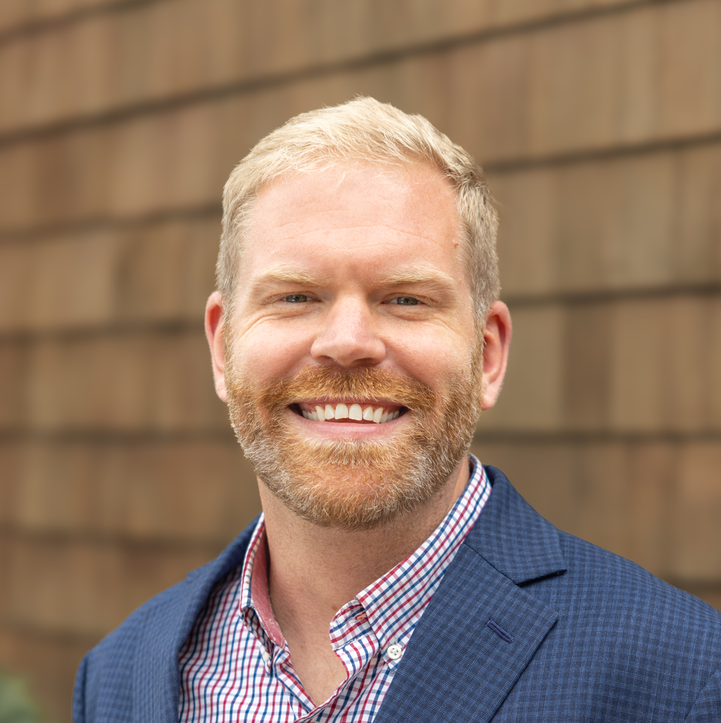 Professional headshot of Jason Veenstra, REALTOR® and team leader of the Veenstra Team, smiling and wearing a blue blazer with a checkered shirt, conveying a friendly, trustworthy, and approachable real estate professional.