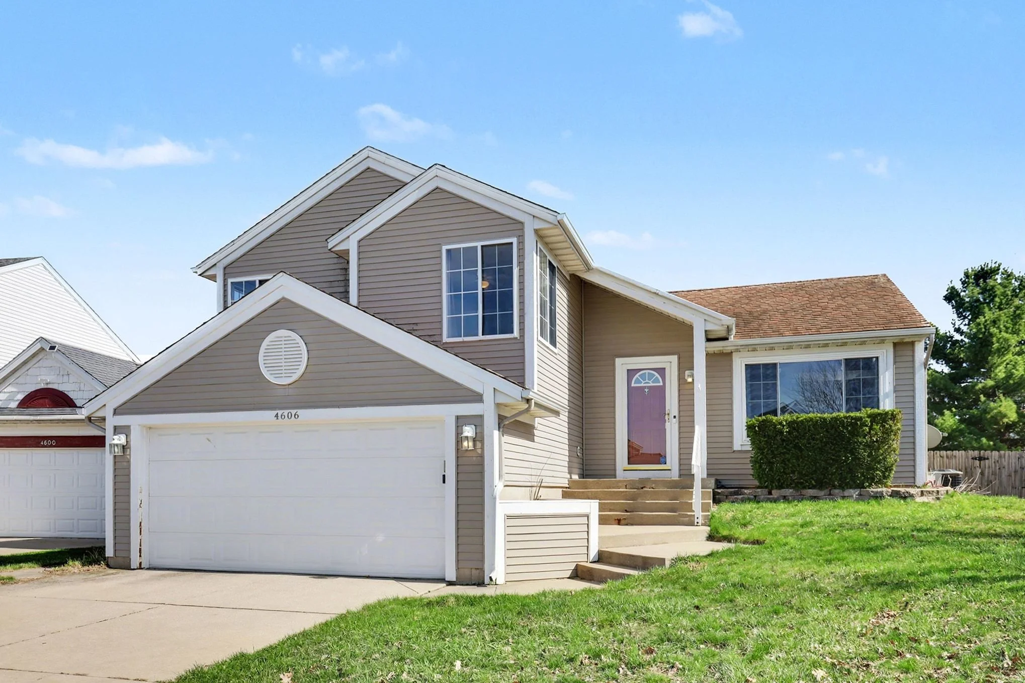 Front exterior of 4606 Country Hill Dr SE in Kentwood, MI featuring a multi-level home with attached two-car garage, tan vinyl siding, white trim, gabled rooflines, front entry with steps, and a well-kept lawn in a quiet residential neighborhood.