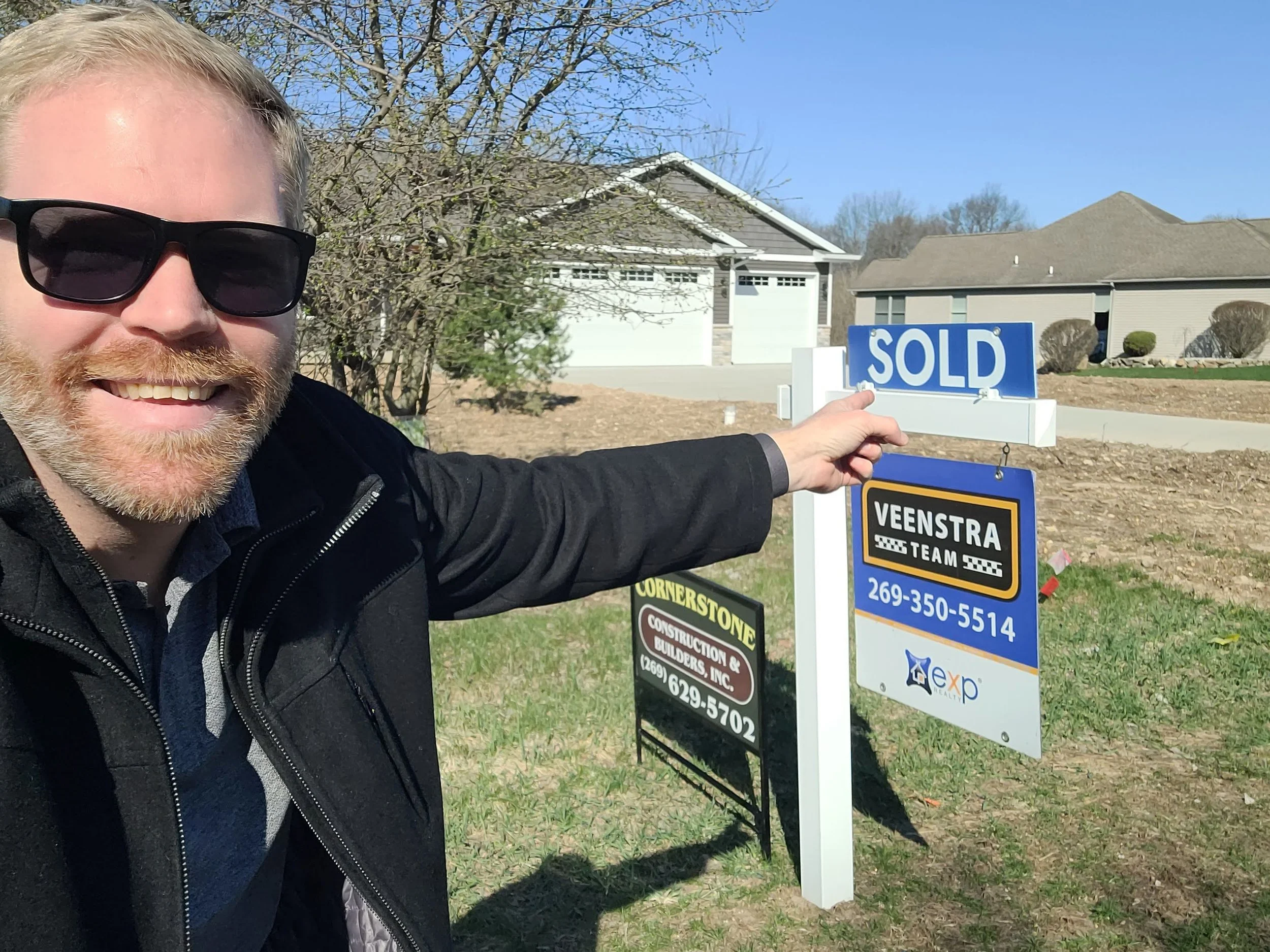 Jason Veenstra standing in front of a sold sign at 8683 Camomile Drive in Augusta, Michigan, a new construction home near Kalamazoo and Gull Lake partially hidden by a tree.