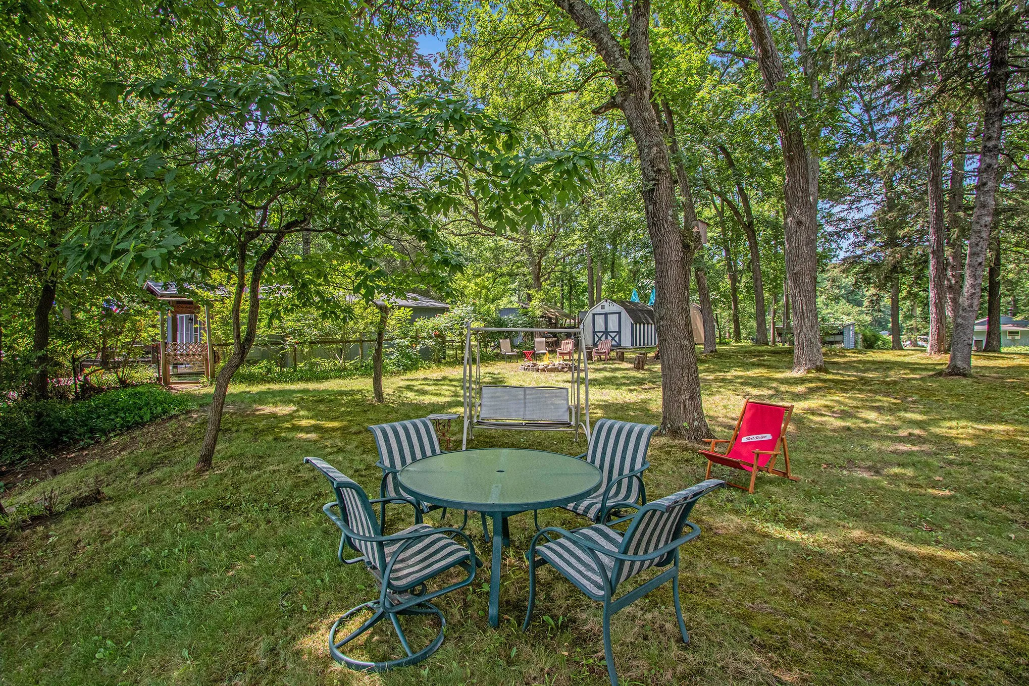 Shaded outdoor dining area beneath mature trees at 14931 Bachelor Island, with a table and chairs on the spacious wooded side lot.