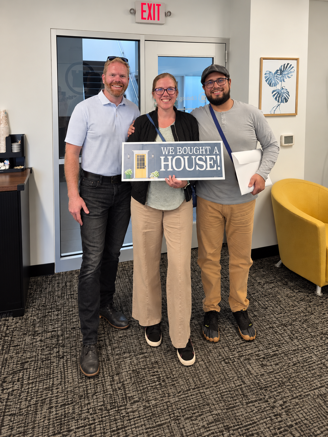 Jason Veenstra poses with Joel and Annette after they closed on their home in Wyoming, Michigan. Annette holds a “We Bought a House!” sign.
