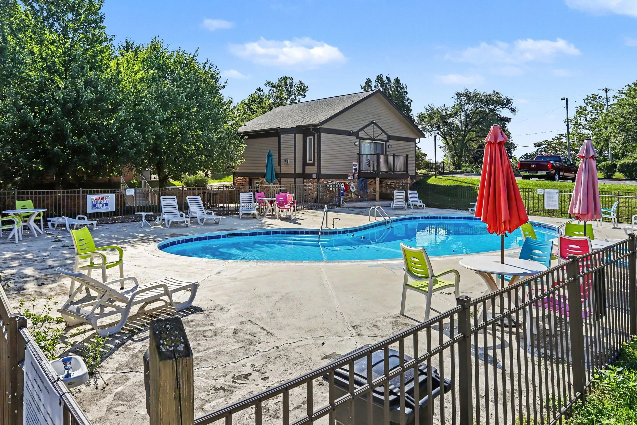 Picture of the kidney bean shaped pool and concrete pation and clubhouse in the background at The gorgeous pool, patio and Clubhouse that you have the right to use when you own 742 W Kilgore #108 Kalamazoo MI