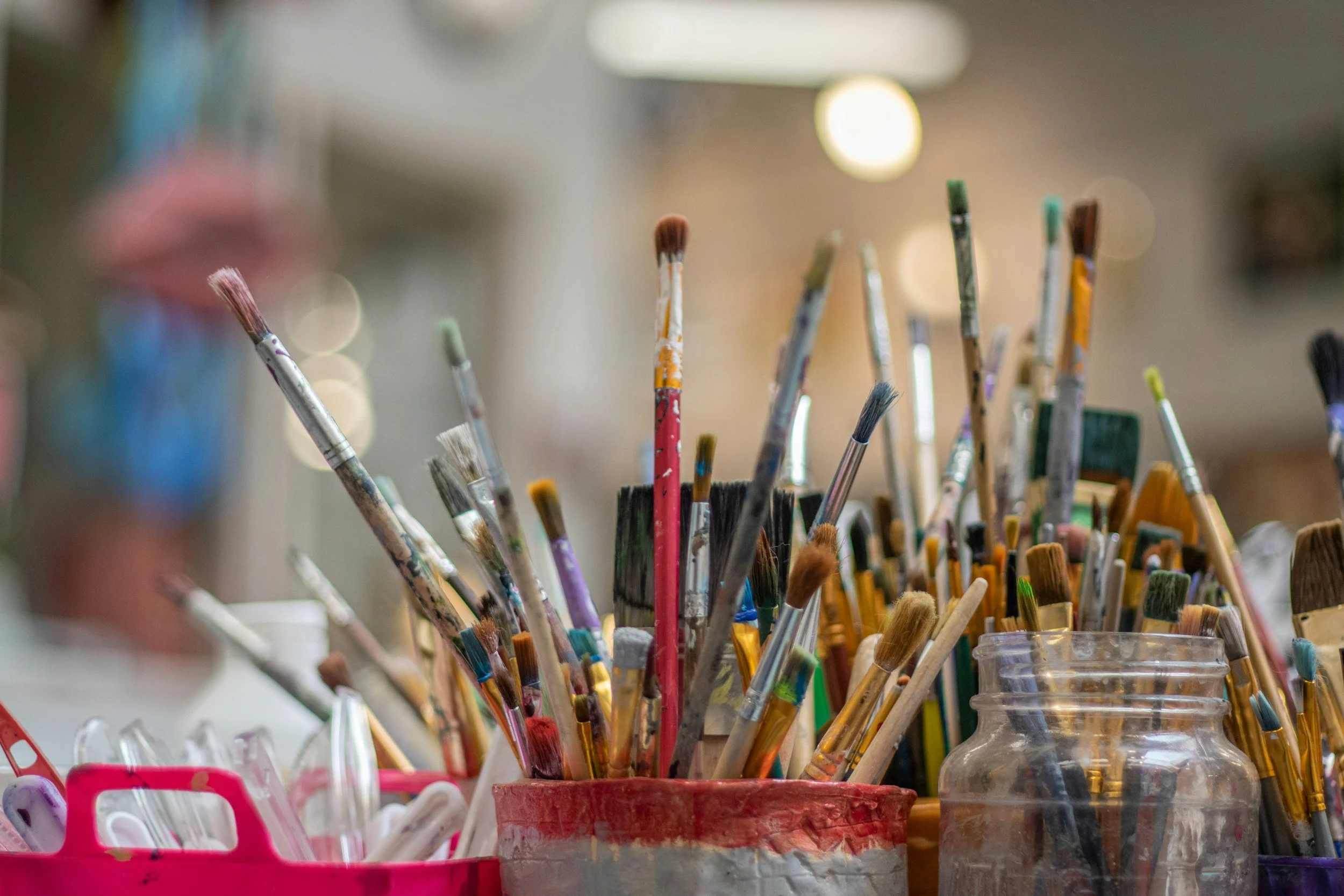 Photo of many paintbrushes sticking upwards out of jars and cans where they have been put to dry. There are more than 30 small brushes available, ready for a classroom of painters to start creating.