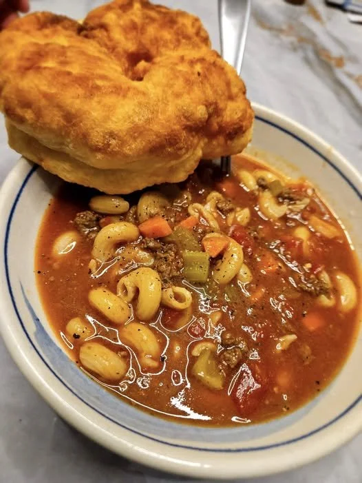 A bowl of soup and fried bannock. The soup looks rich and chunky with tomatos, vegetables and macaroni.