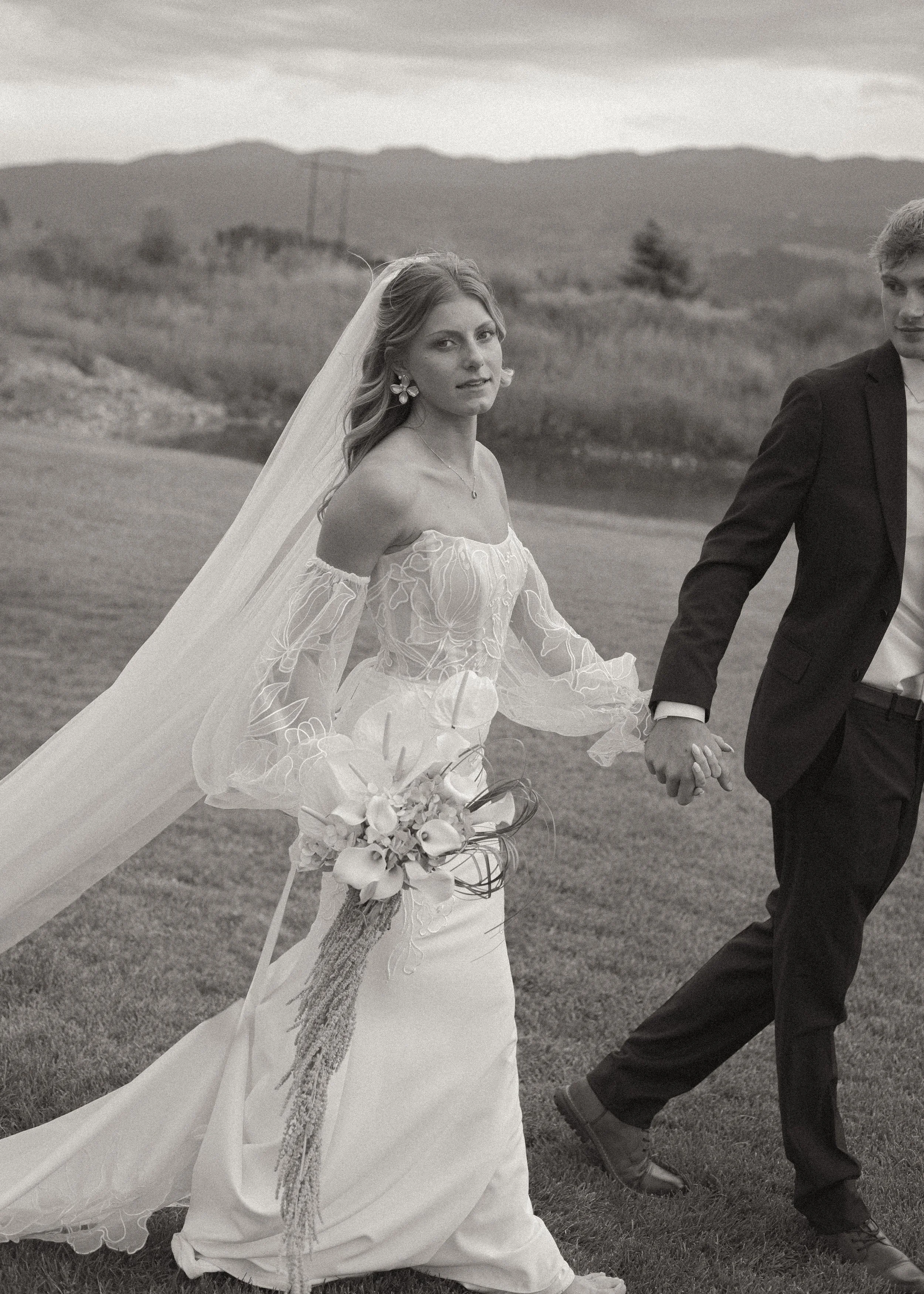 Black and white photo of bride and groom walking hand in hand.