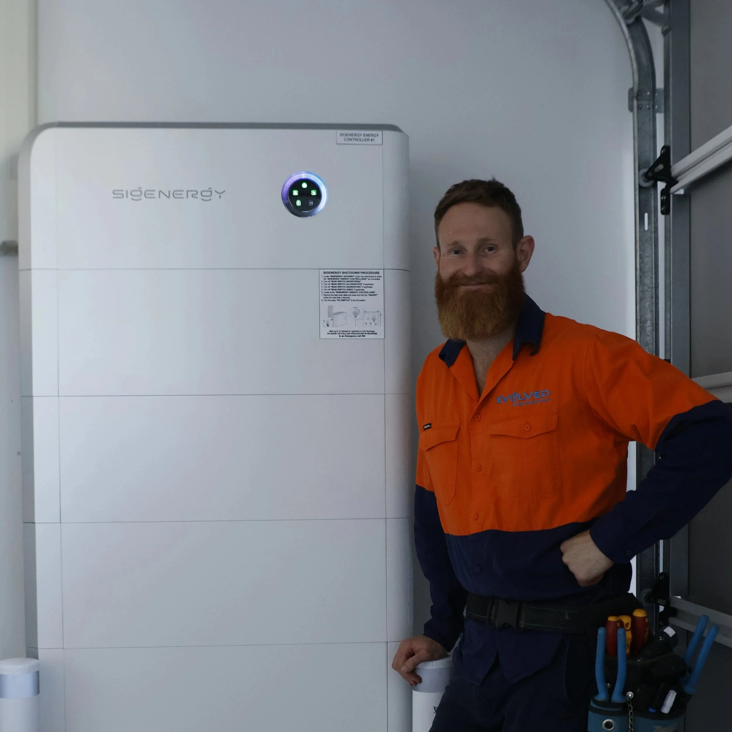 Steven Hord, Master Electrician, standing next to a large white energy storage unit in a facility.