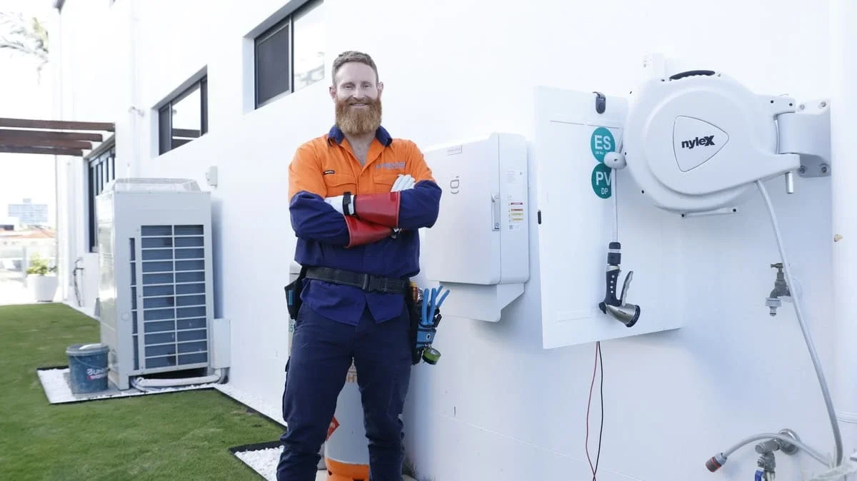 Steven, licensed Master Electrician at Evolved Solar & Electrical, standing beside a completed solar switchboard installation on the Gold Coast