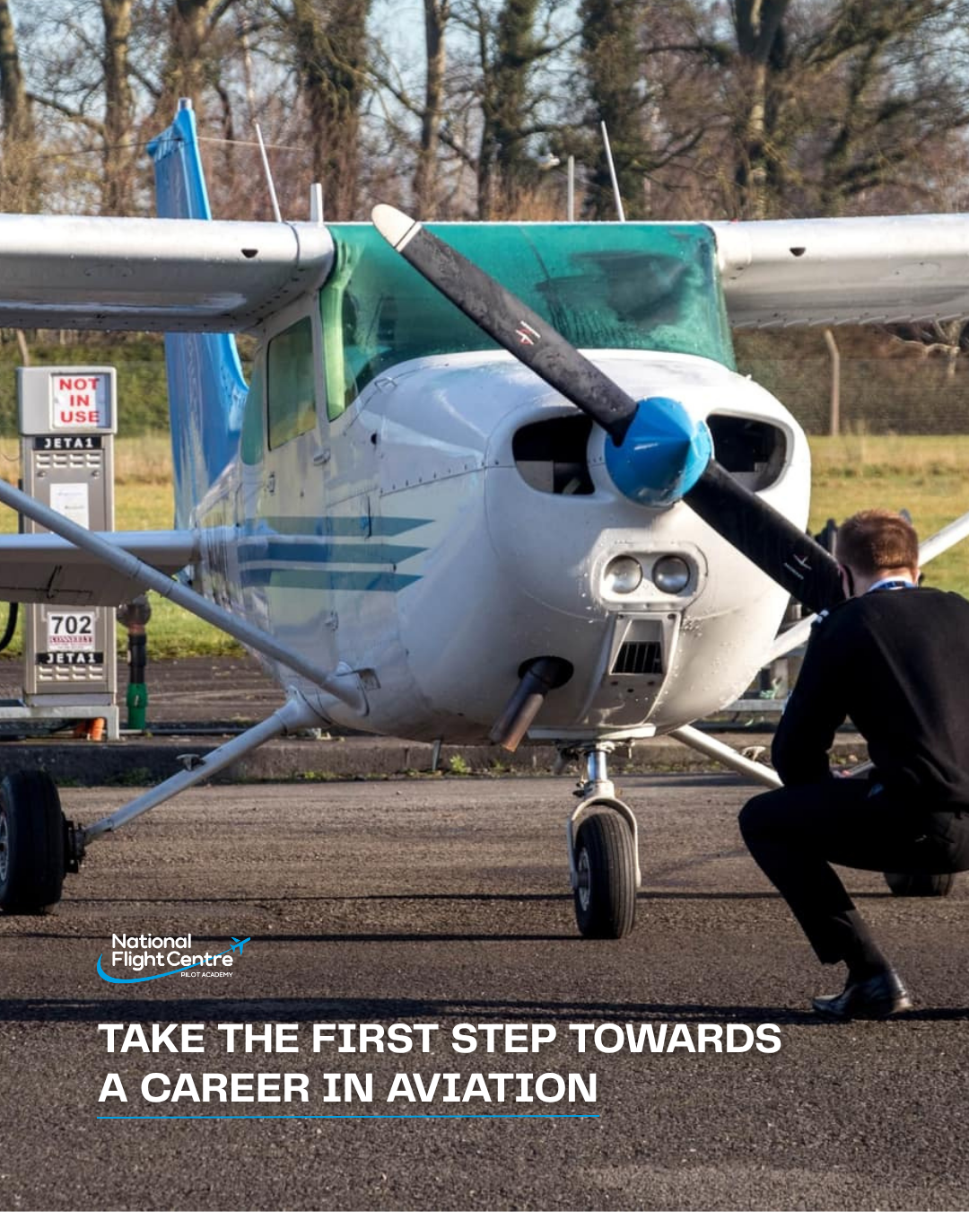 A small airplane on a tarmac with a person in a suit squatting next to it, touching the propeller, and a sign in the background that says 'NOT IN USE'.
