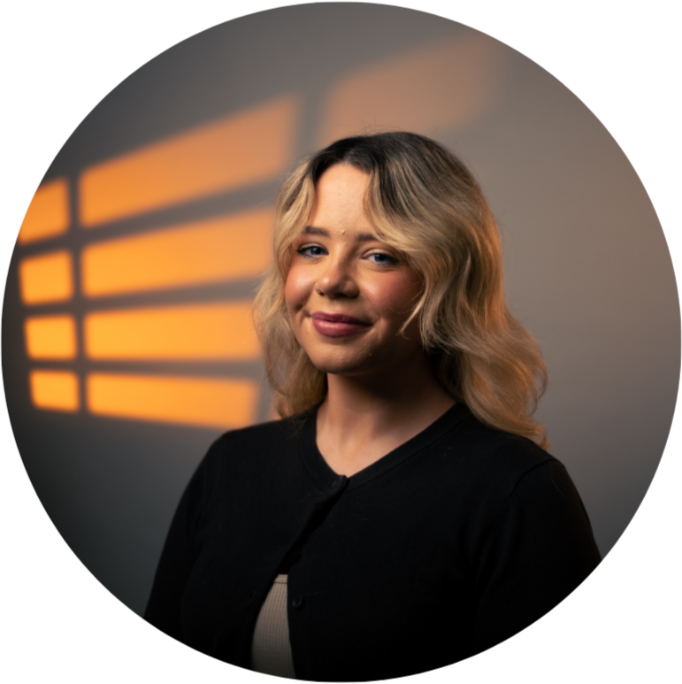Smiling woman with blonde hair, wearing a black top, against a dark background.