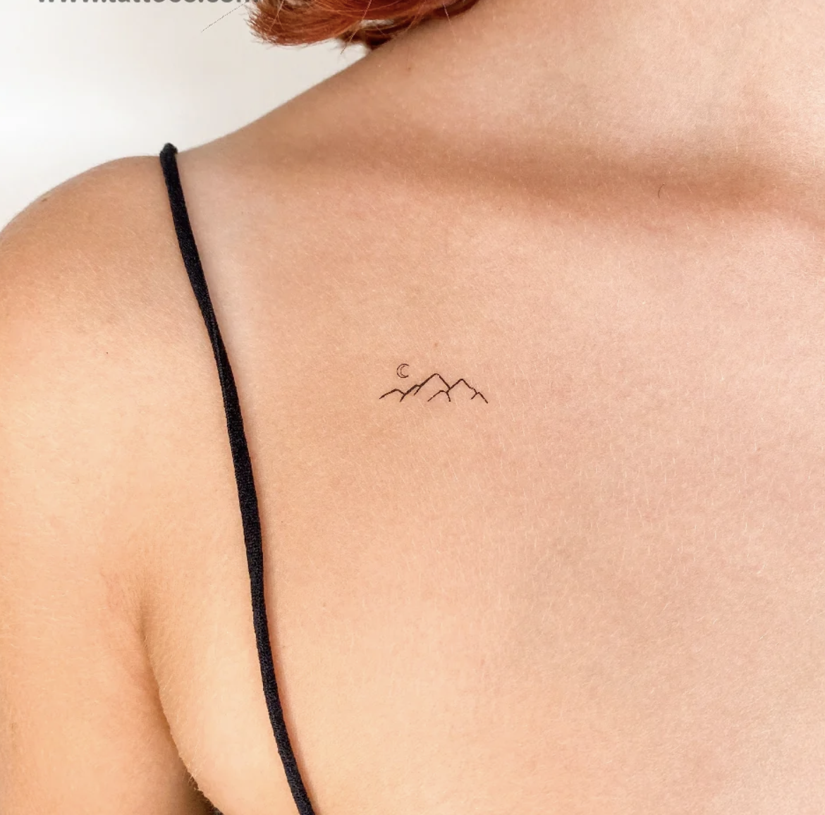 Small minimalist tattoo of mountain peaks with a crescent moon on the upper left, on a person's upper chest near the shoulder.