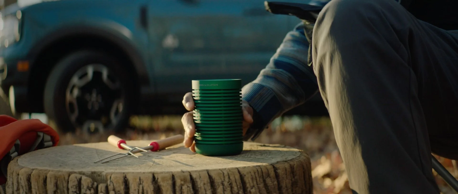 Beosound Explore portable speaker on a log with Ford Bronco Sport in the background.