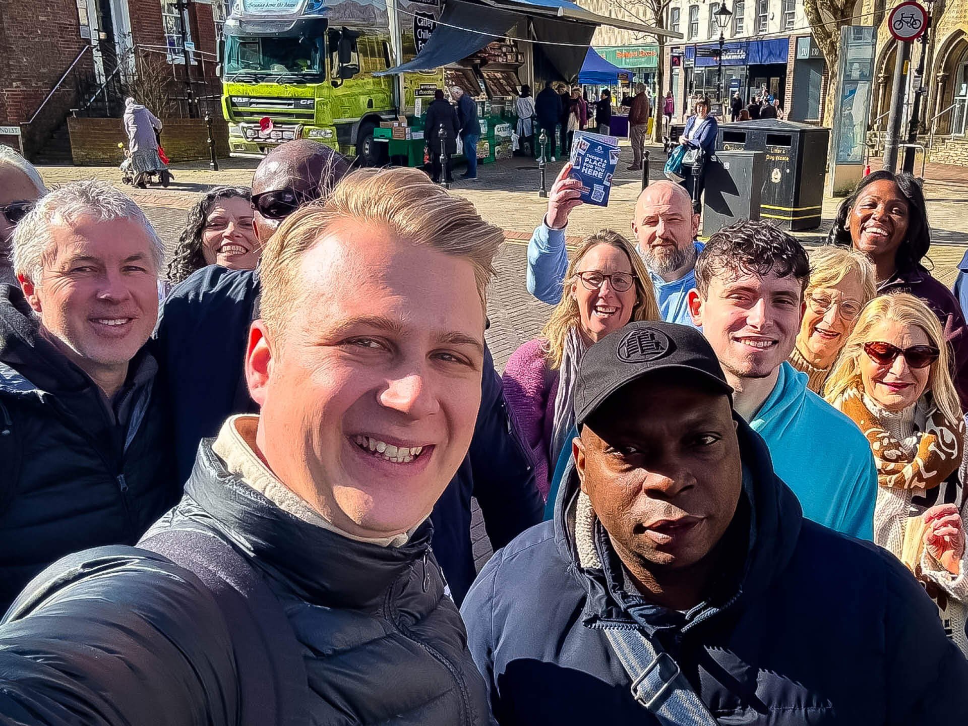 A diverse group of people take a selfie in Poole town centre, with one man holding up flyers as they share about Jesus on the streets.
