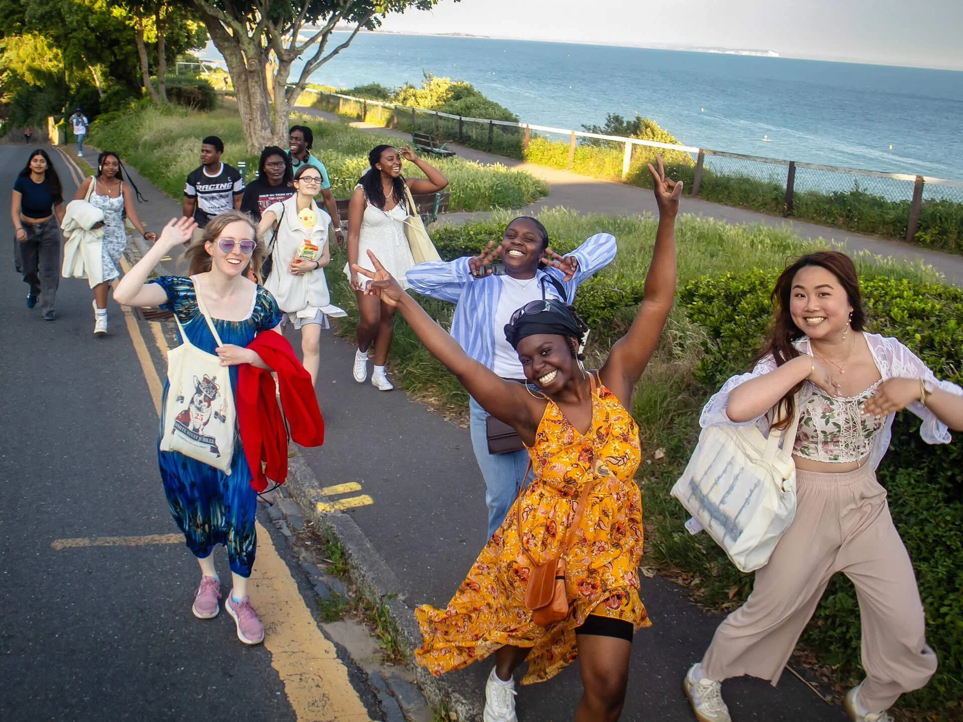 A multicultural group of Christian students and young adults walking along Bournemouth beach in the sunshine, smiling and posing for the camera on their way to Bangers and Mosh—Citygate students’ end-of-year party.