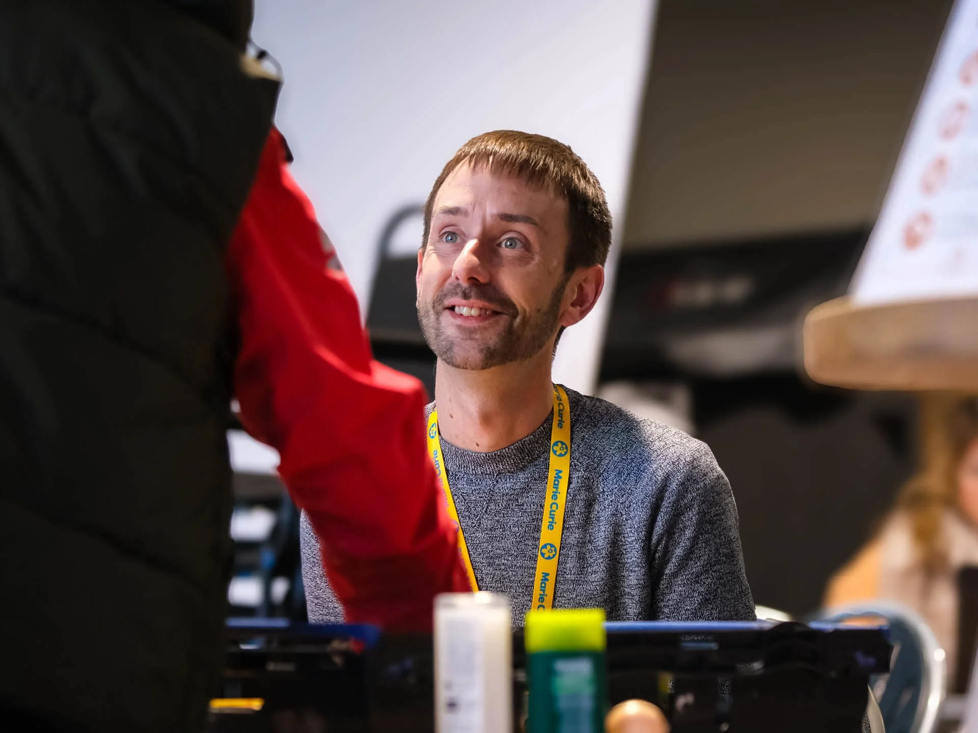 A seated man in his early 30s smiles at someone collecting a food parcel from the Citygate Community Hub.