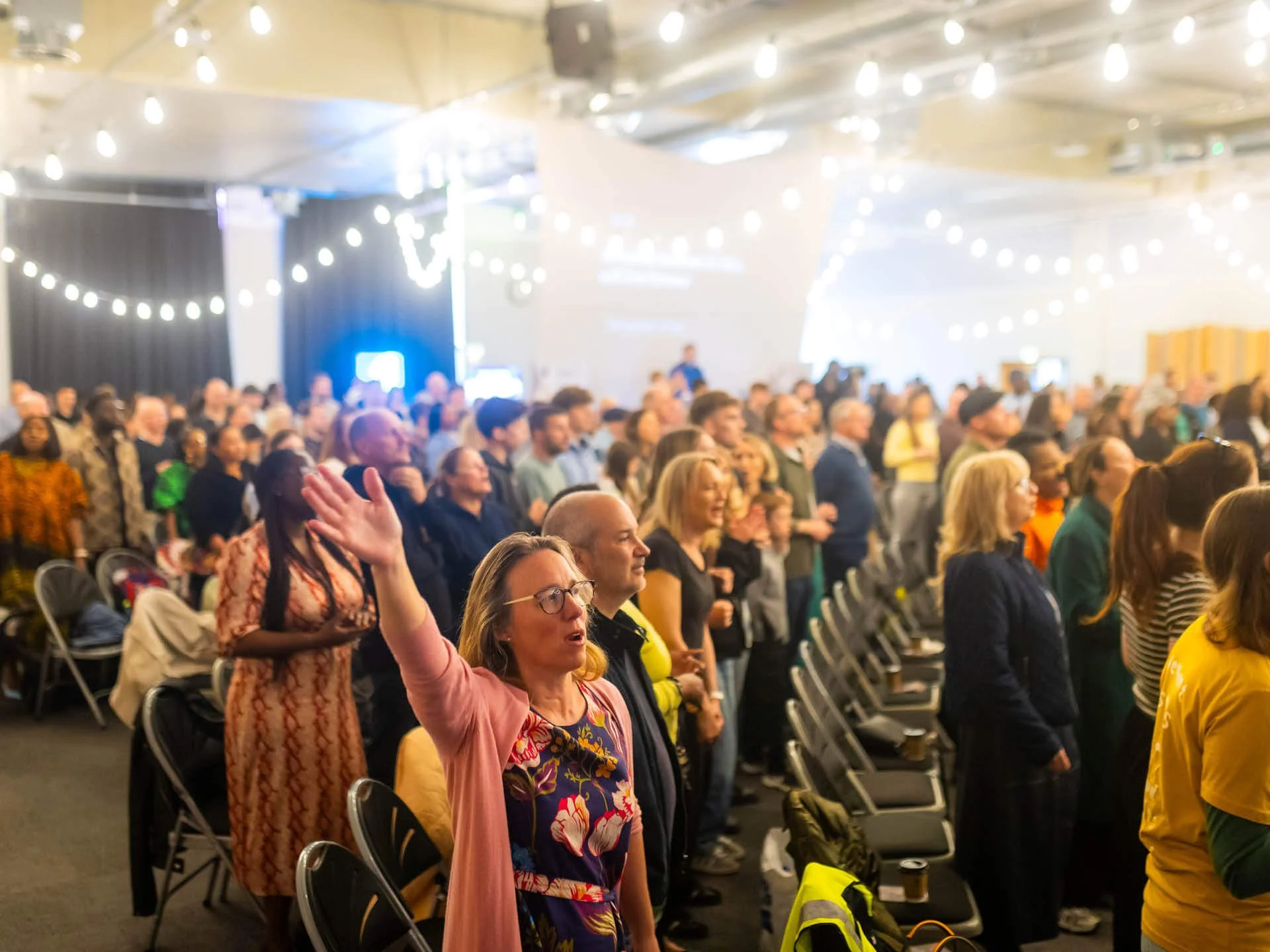 Wide-angle shot of the diverse Bournemouth congregation, many with their hands raised in worship.
