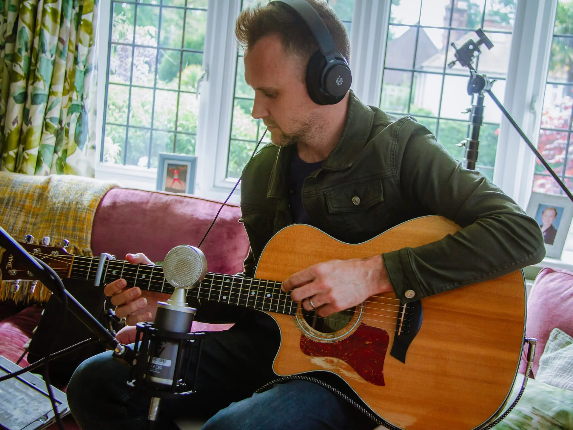 White man playing guitar with headphones on and a mic
