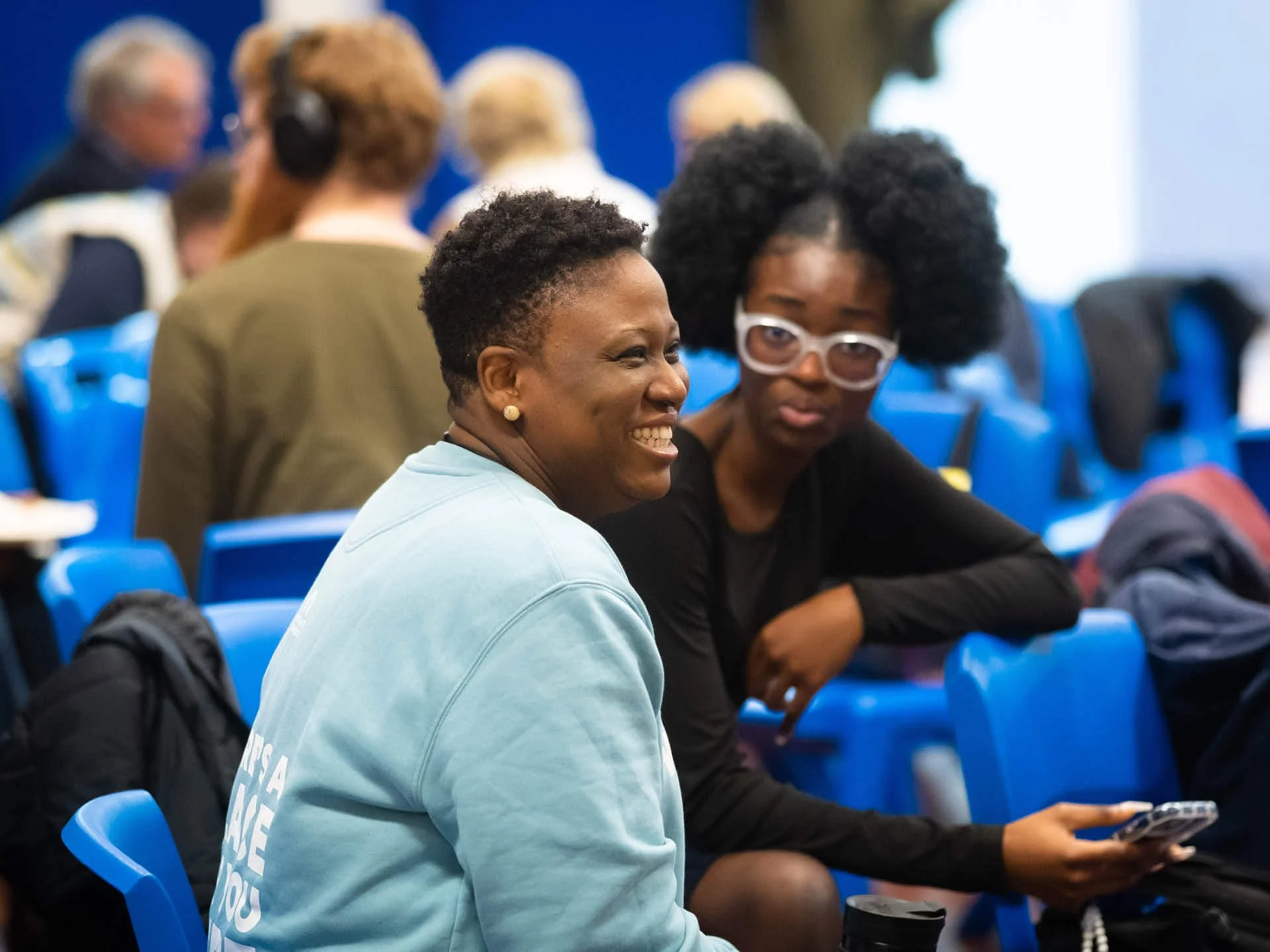 A woman sits in a church service, smiling warmly with her teenage daughter beside her.