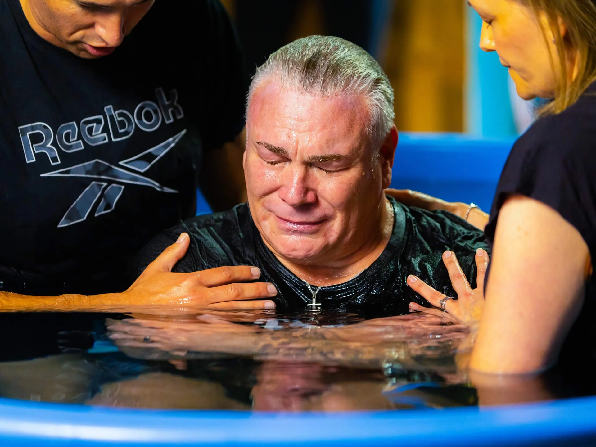 A man is getting baptized at church - he's emotional and touched as two people pray for him.