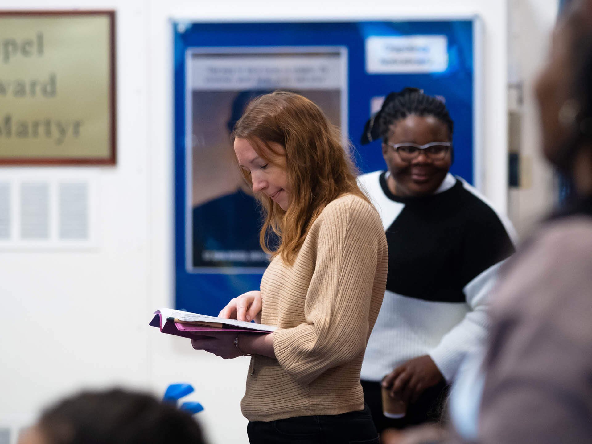 A woman wearing a brown jumper gazes thoughtfully at an open Bible, lost in contemplation.
