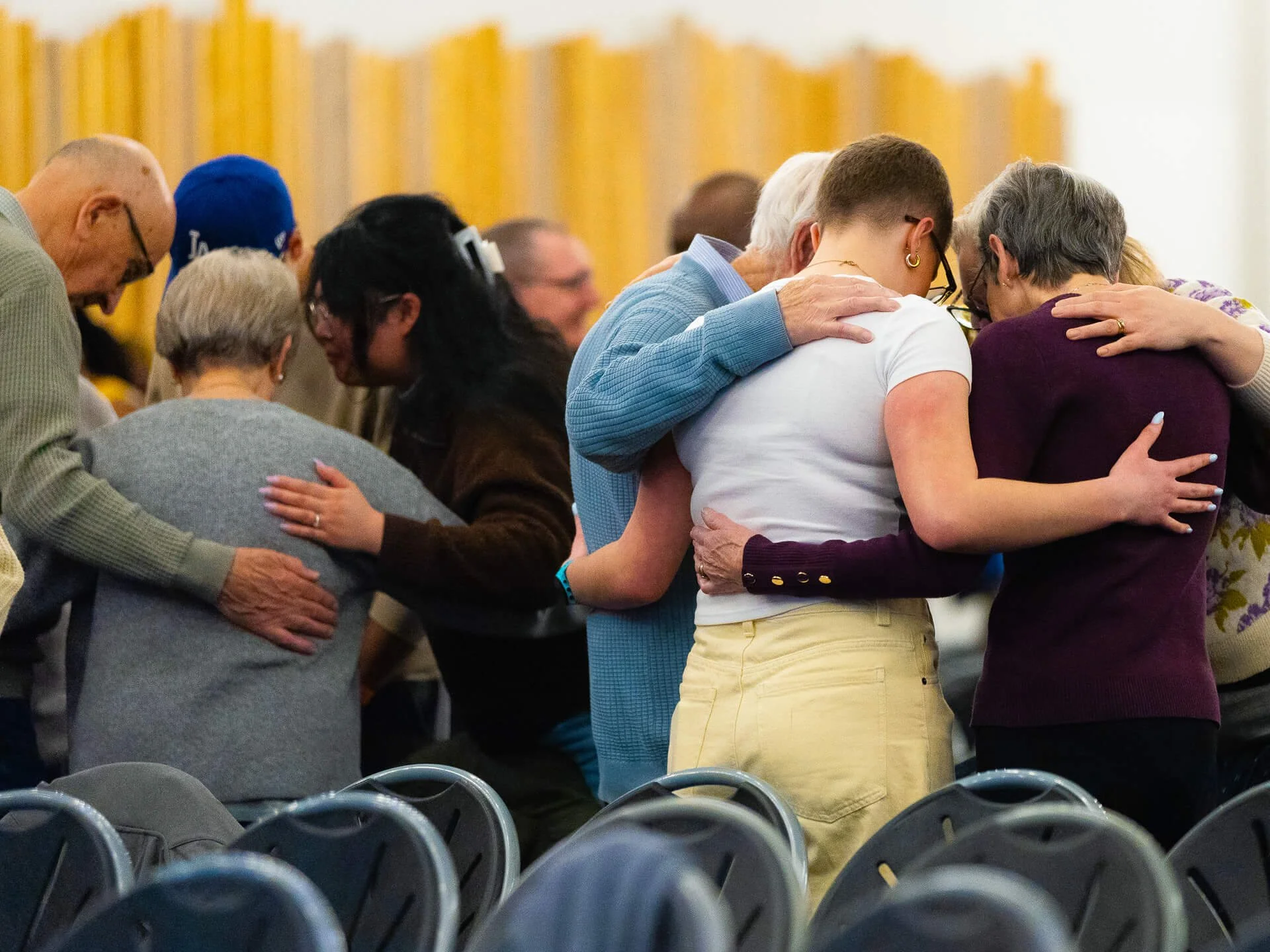 People praying together in small groups at church, with their arms around each other in a circle, showing church family and community.