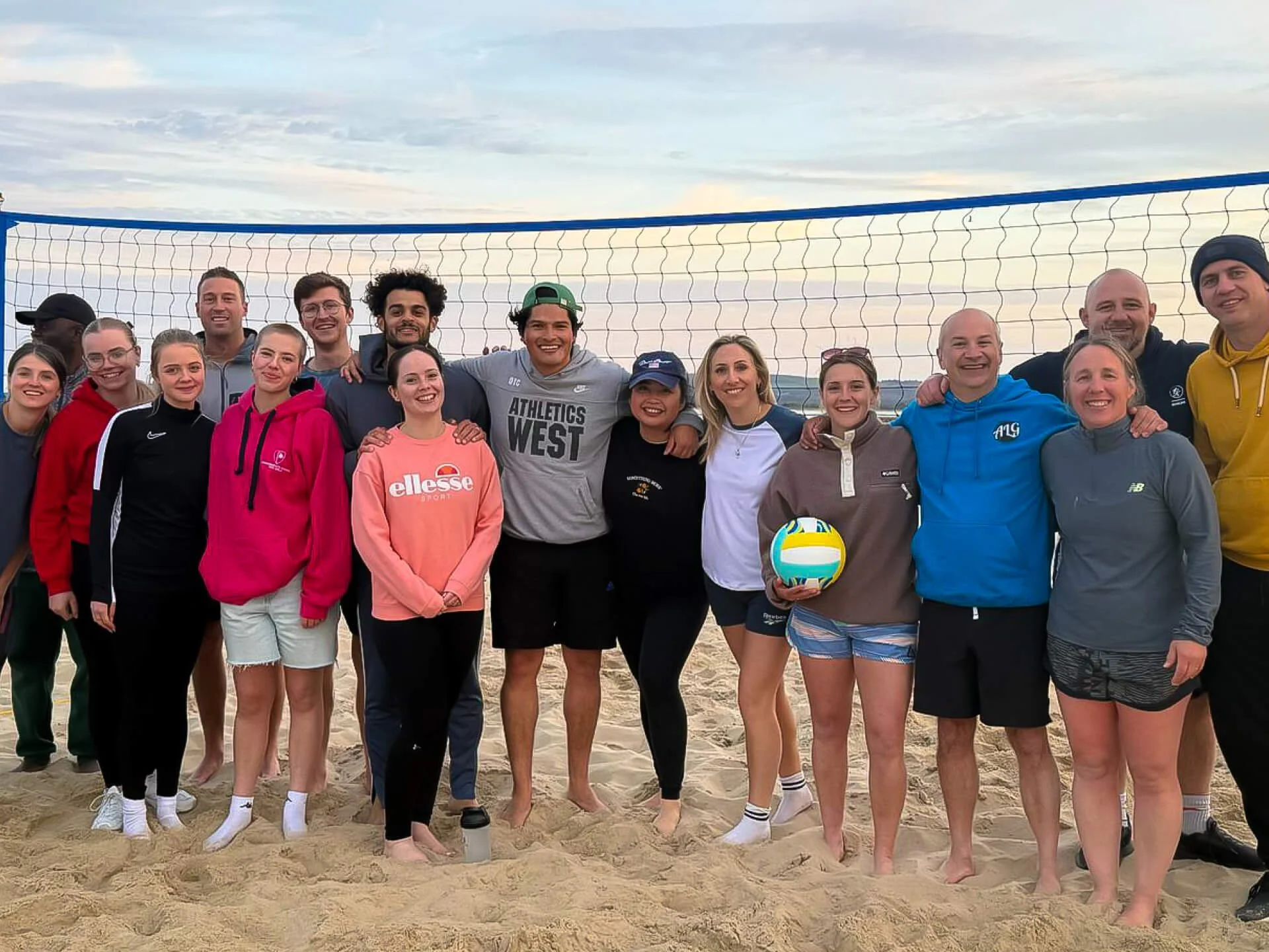 An intergenerational group of smiley people, playing volleyball and hanging out at the beach together, showing friendship and community.