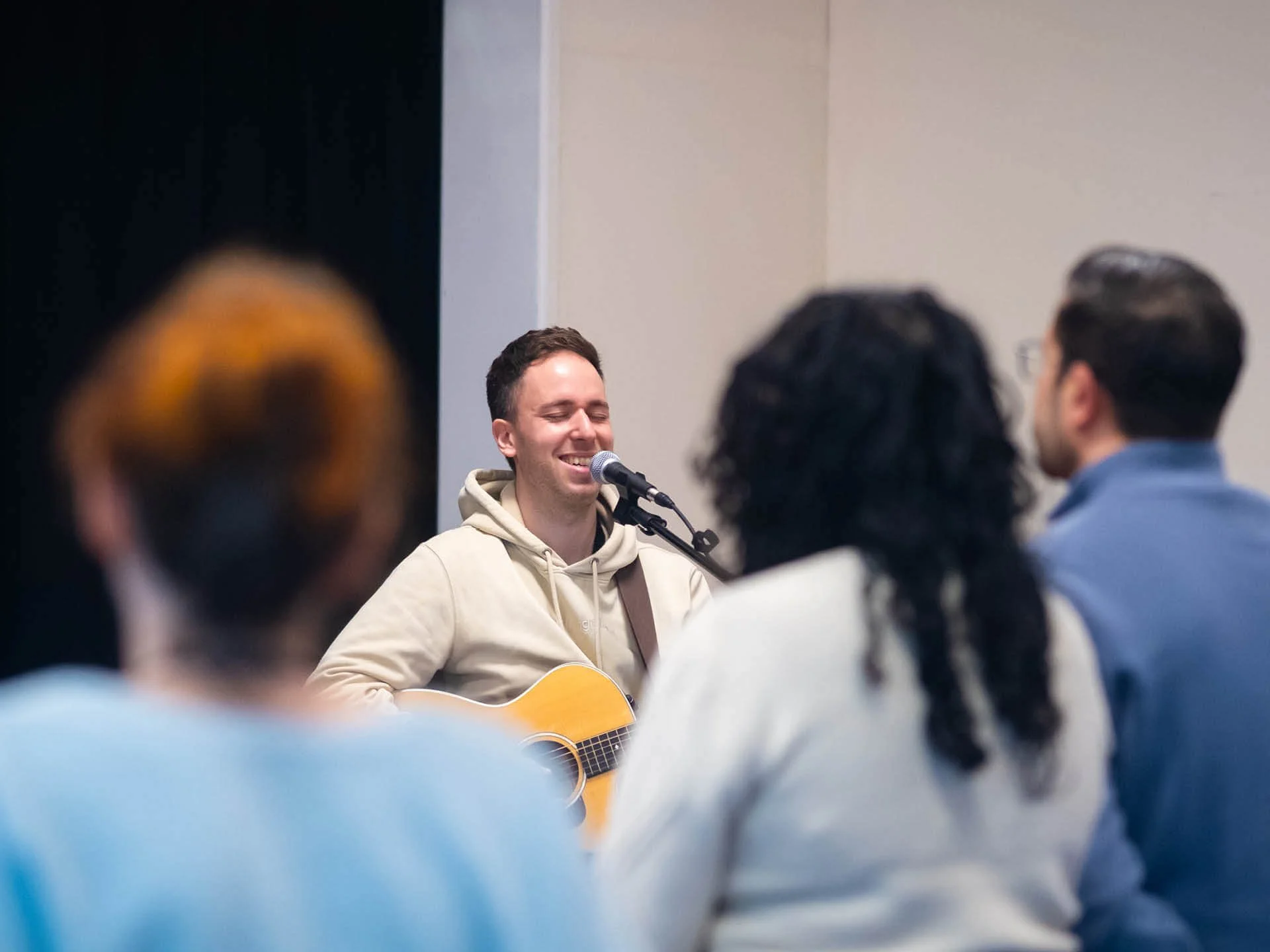 Young man in a cream jumper smiles while playing the guitar during a church meeting.
