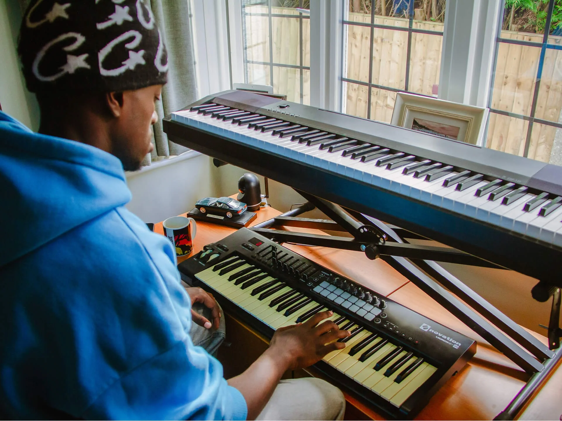 Black man playing keyboard in a blue hoodie and black beanie