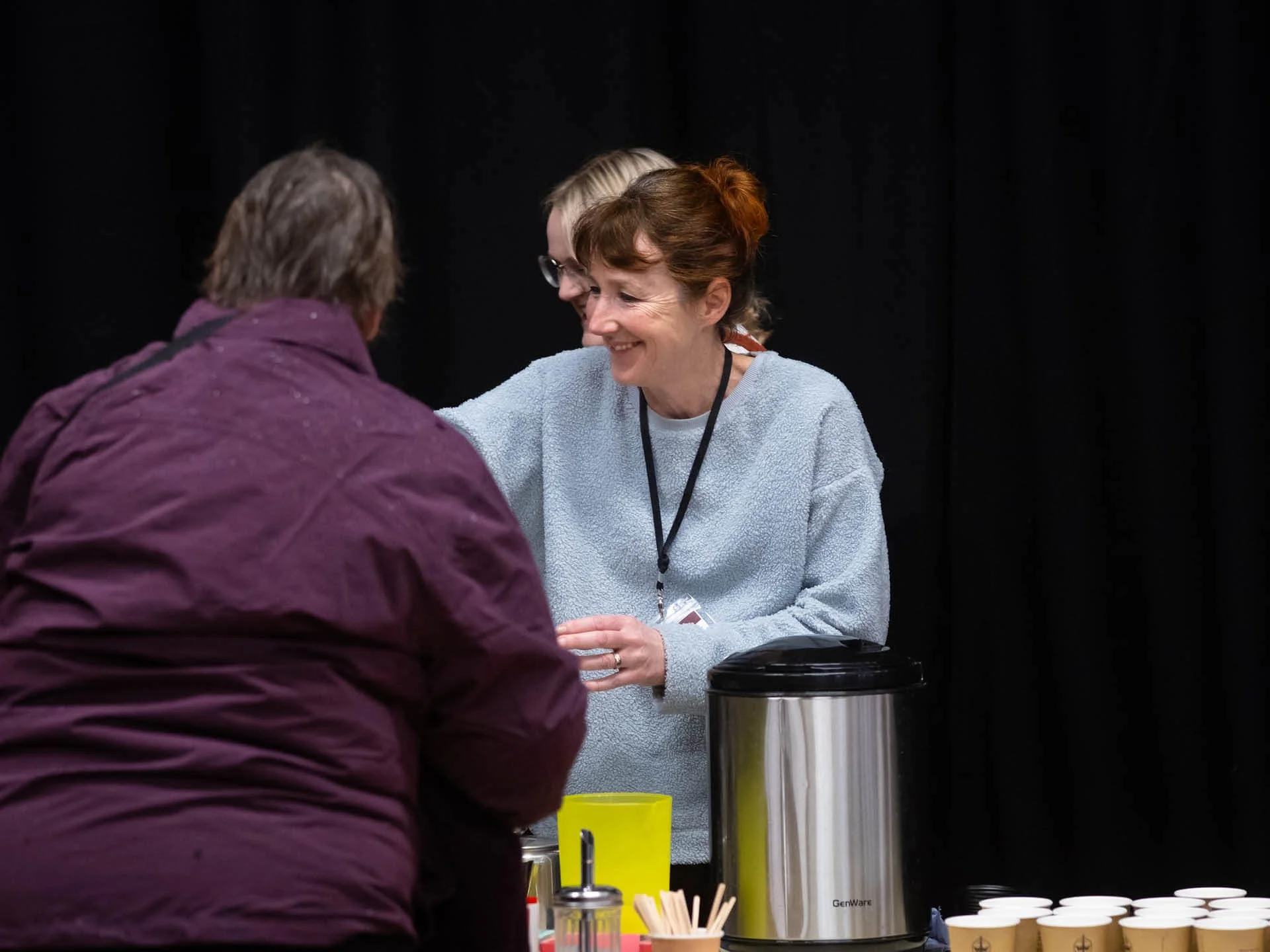 A smiling woman in a blue jumper serves refreshments during a church meeting.