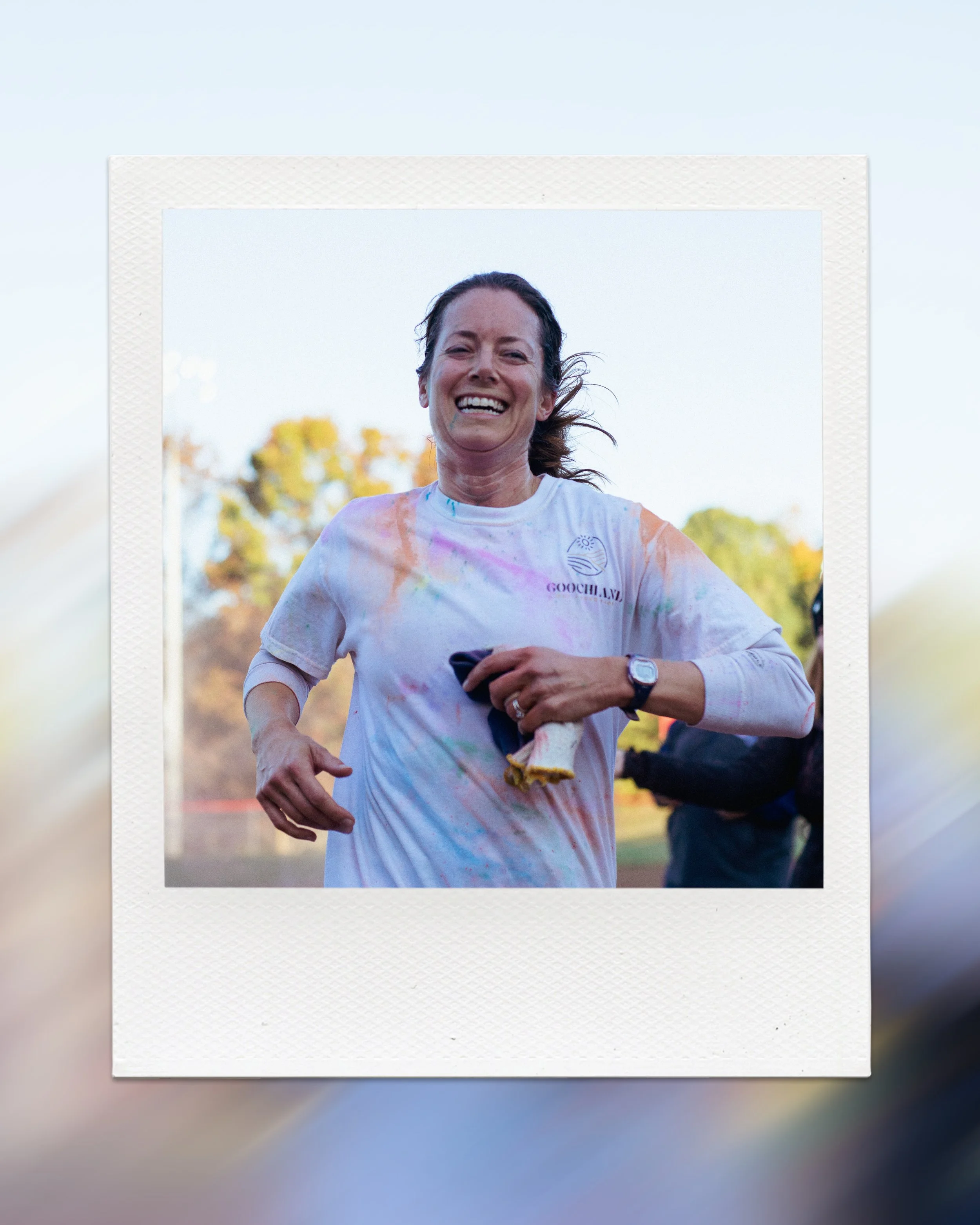 Smiling woman in a white shirt with colorful stains, running outdoors
