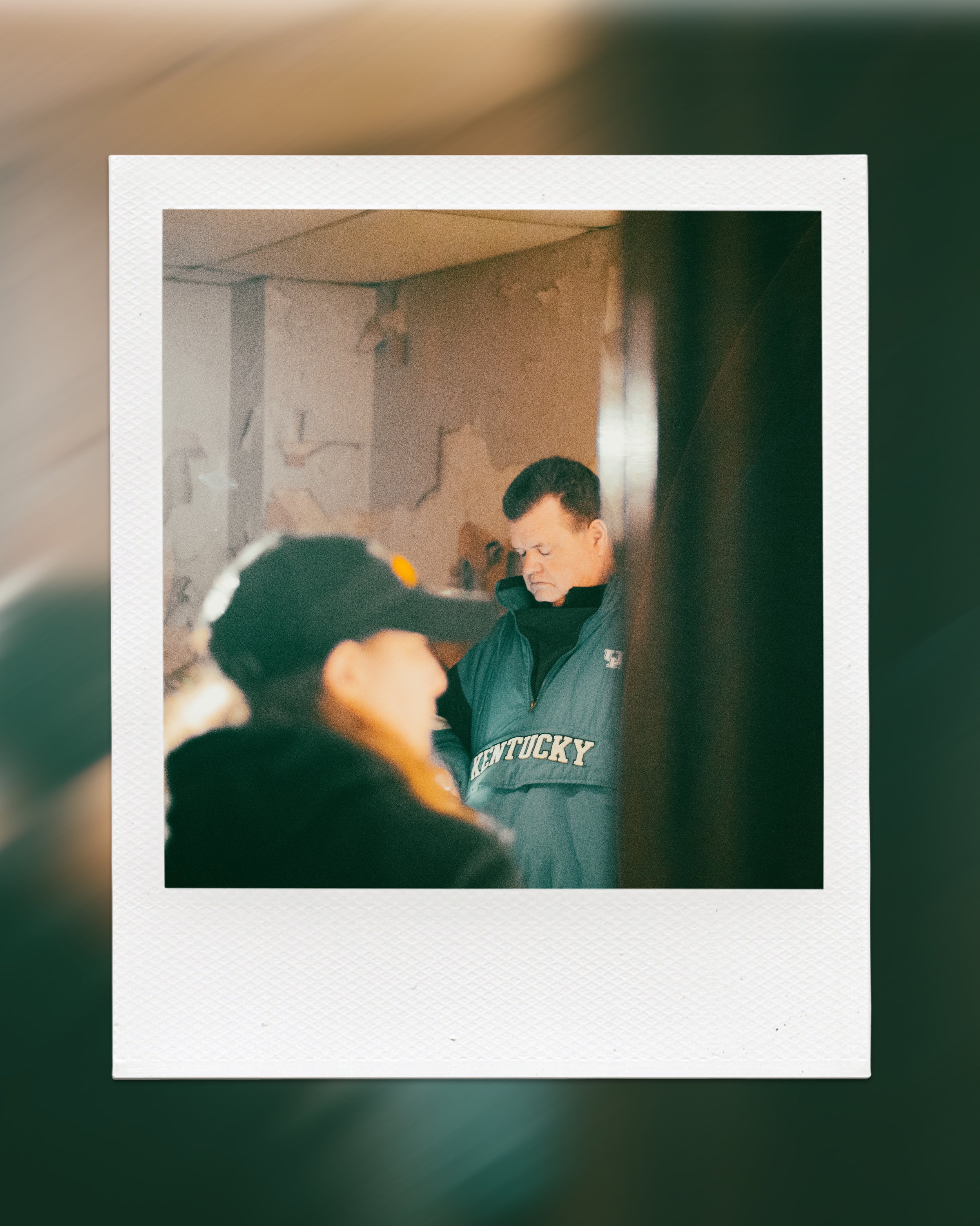 Polaroid photo of an indoor scene with a person wearing a "Kentucky" vest.