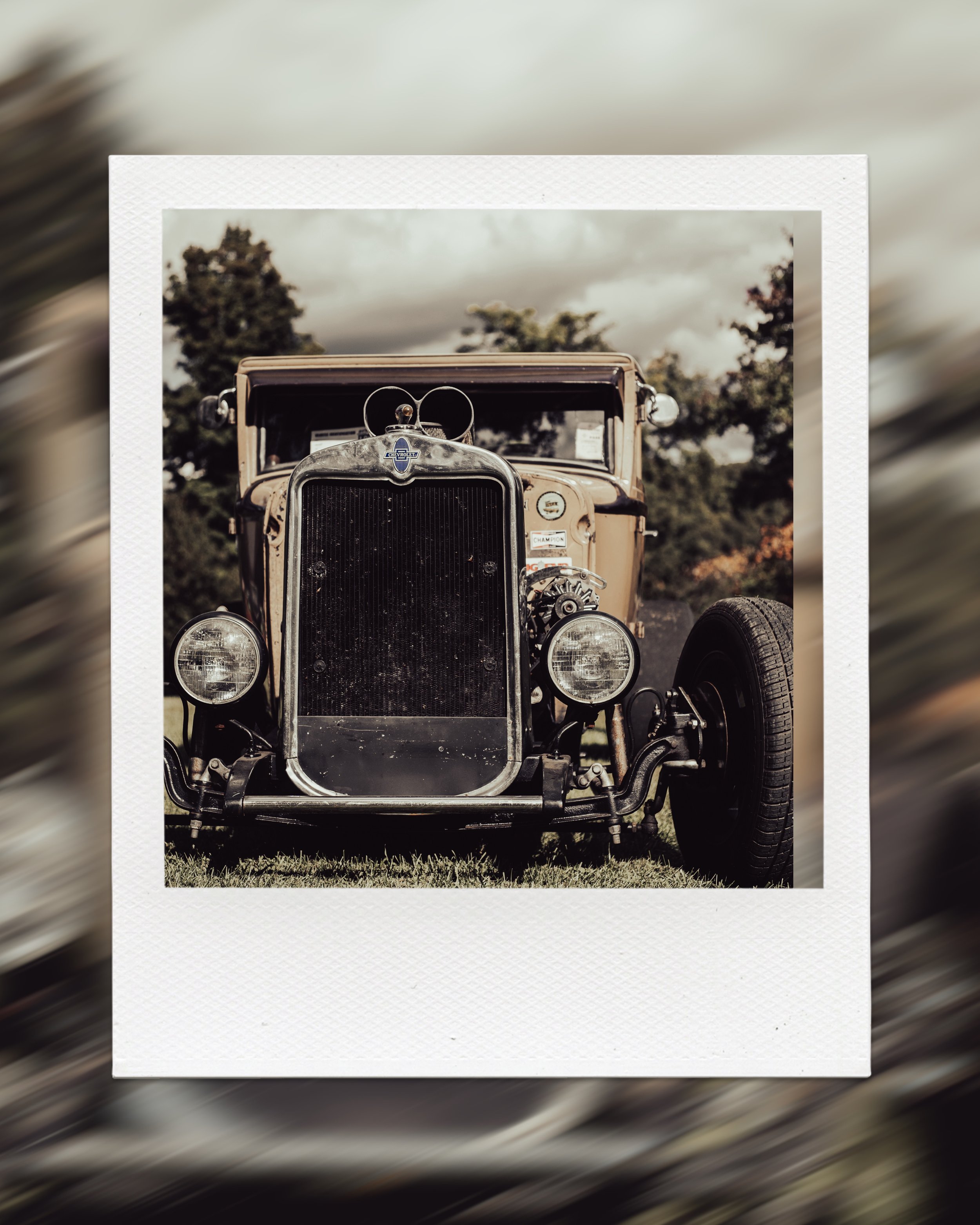 Vintage car front view, classic design, round headlights, radiator grille, green grass, trees in background.