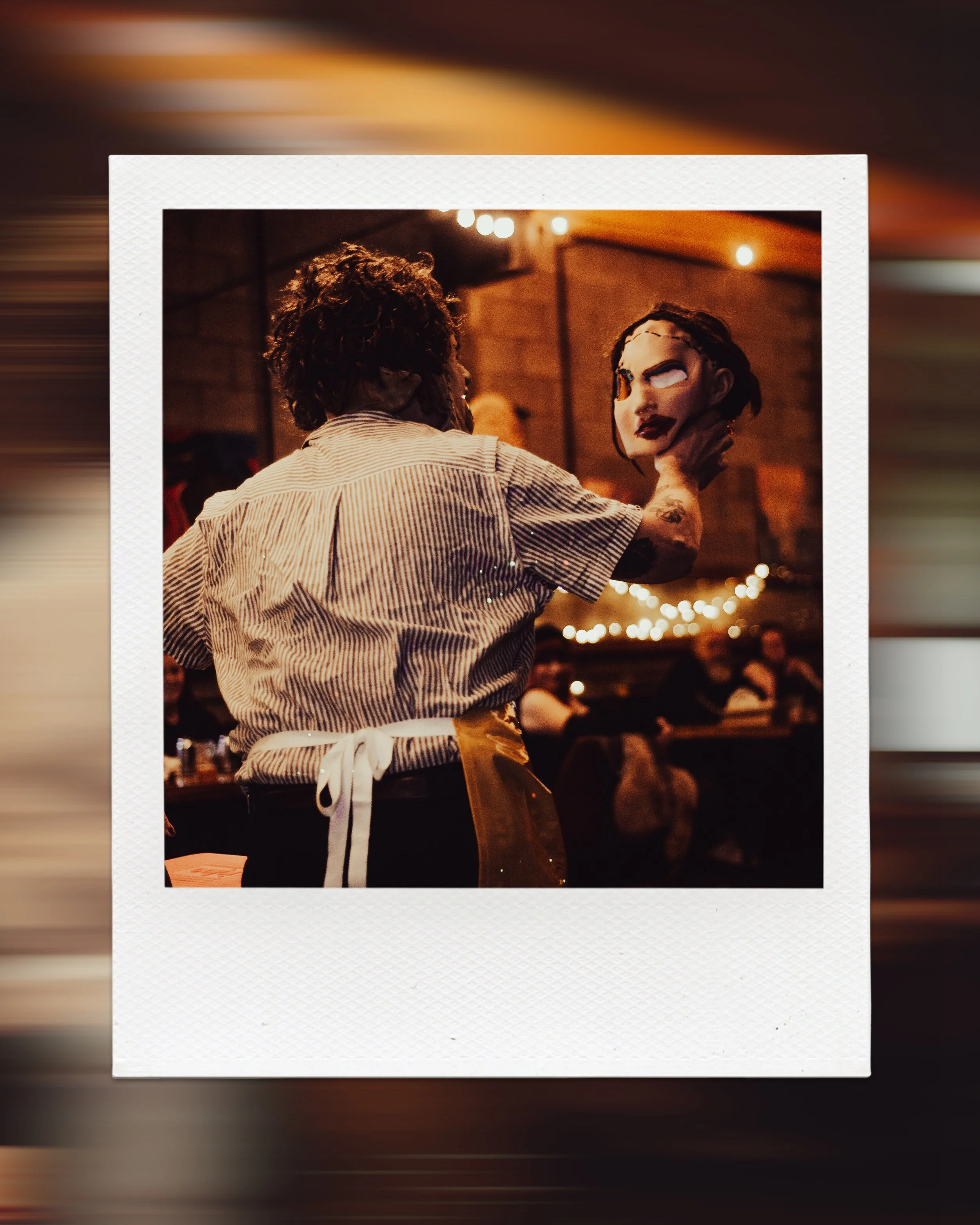 Person holding a mask in a dimly lit room with string lights